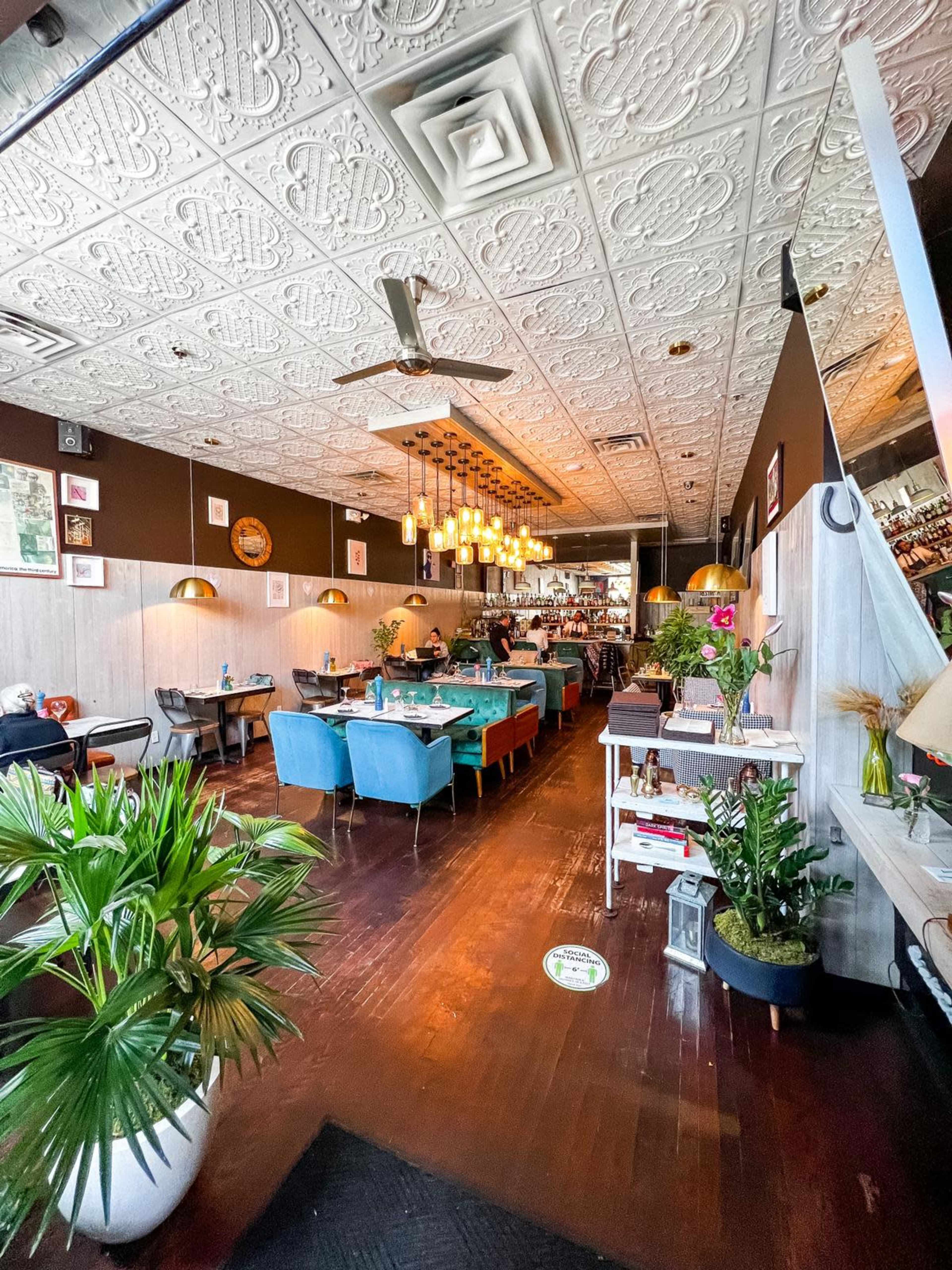 The image shows a restaurant interior featuring a textured ceiling, tables with teal chairs, and warm pendant lighting.