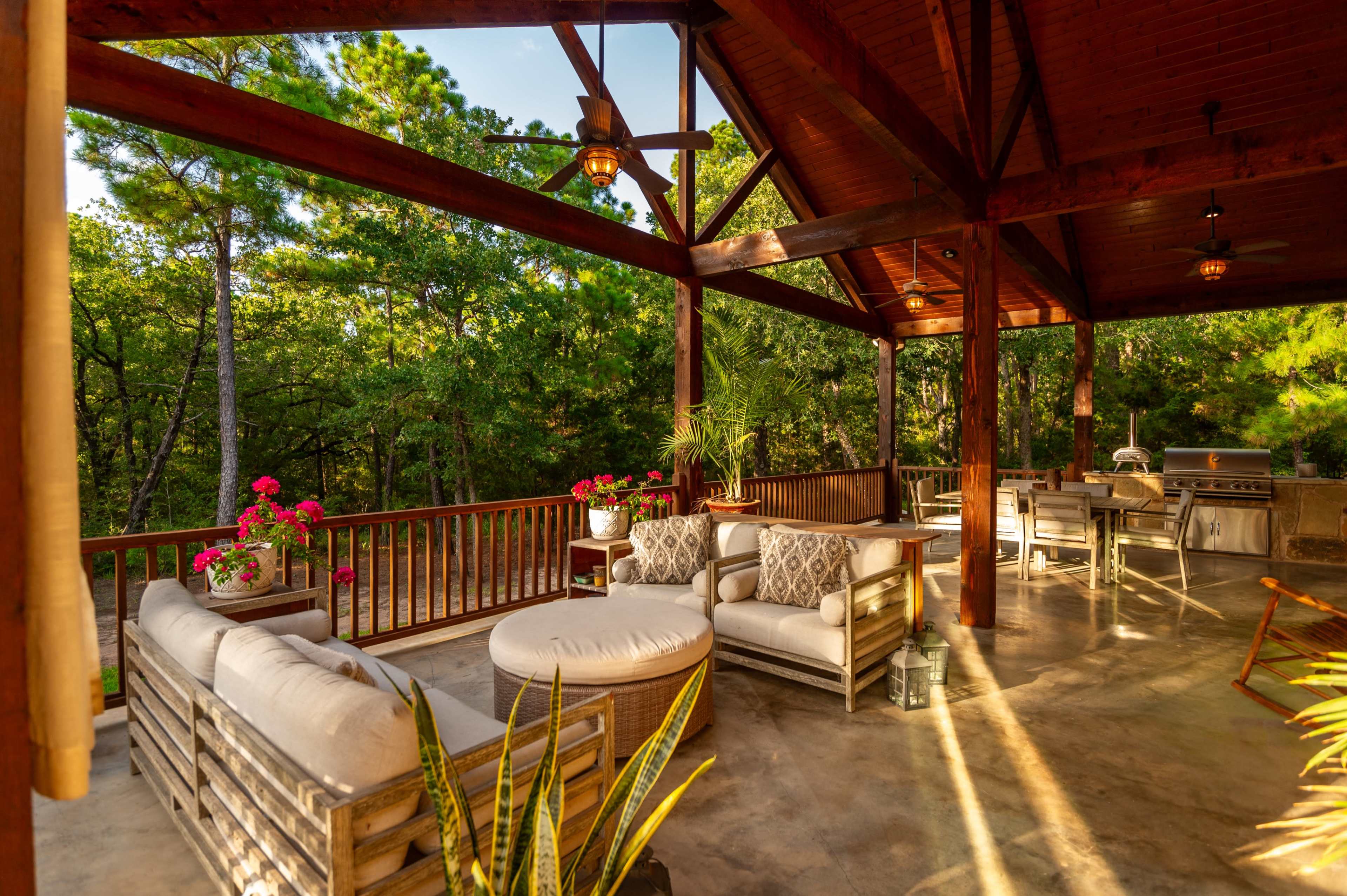 A spacious outdoor patio area with wooden beams, comfortable seating arrangements, and potted plants overlooking a green landscape.
