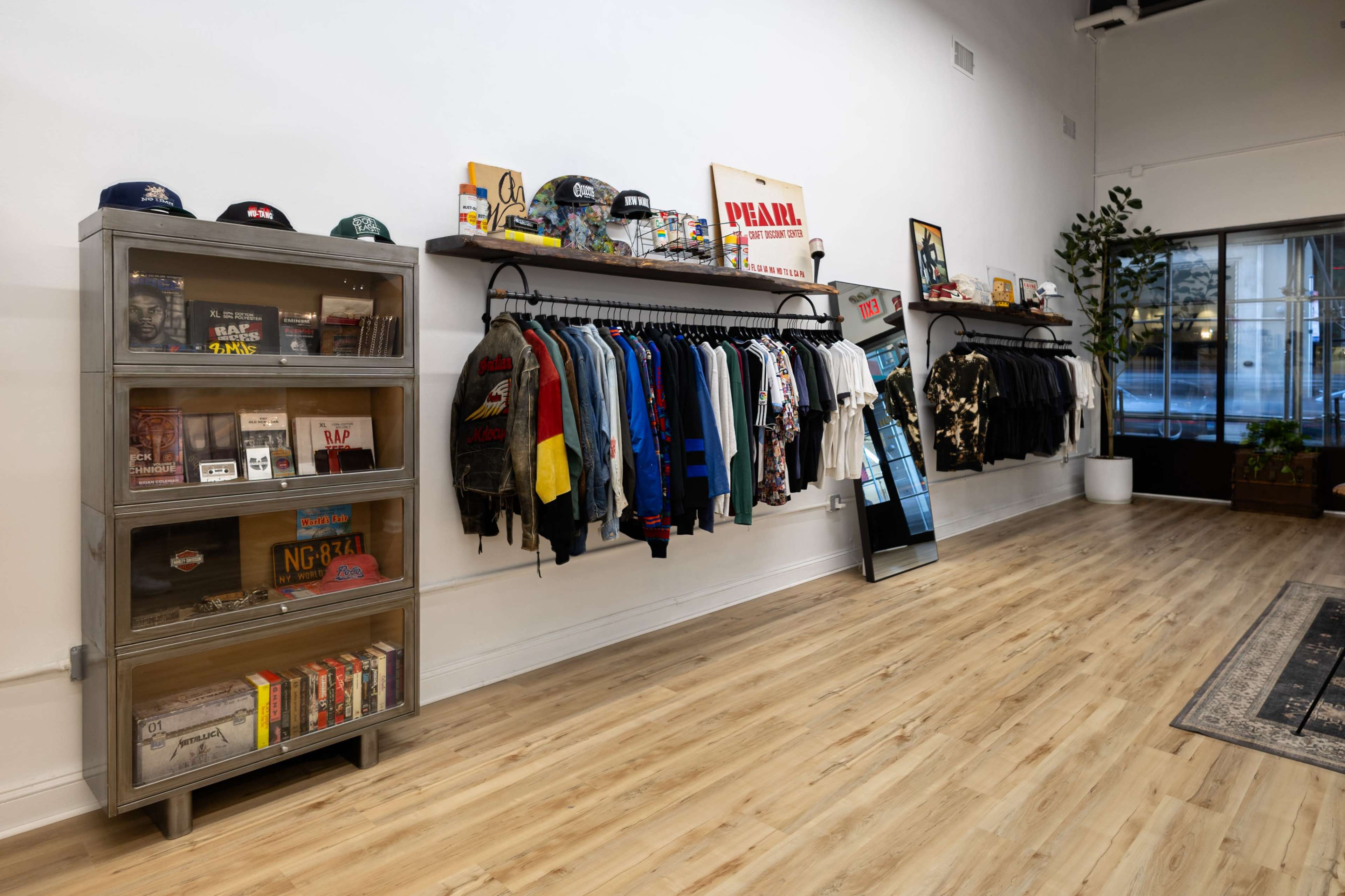 The image shows a retail store interior with clothing racks displaying various garments and a shelf containing books and music items along one wall.