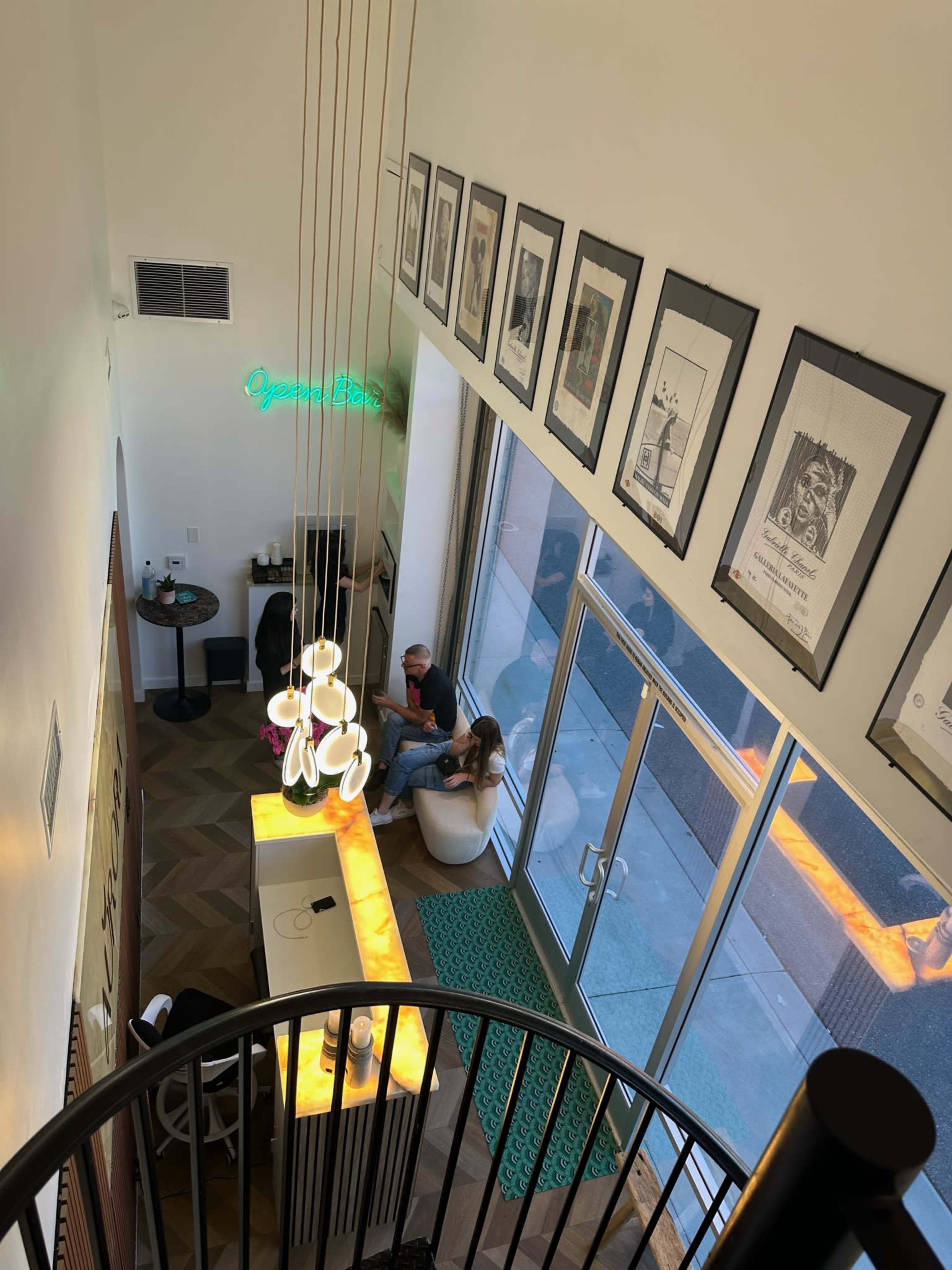 An interior view of a modern café with hanging light fixtures, artwork on the walls, and patrons seated at tables.