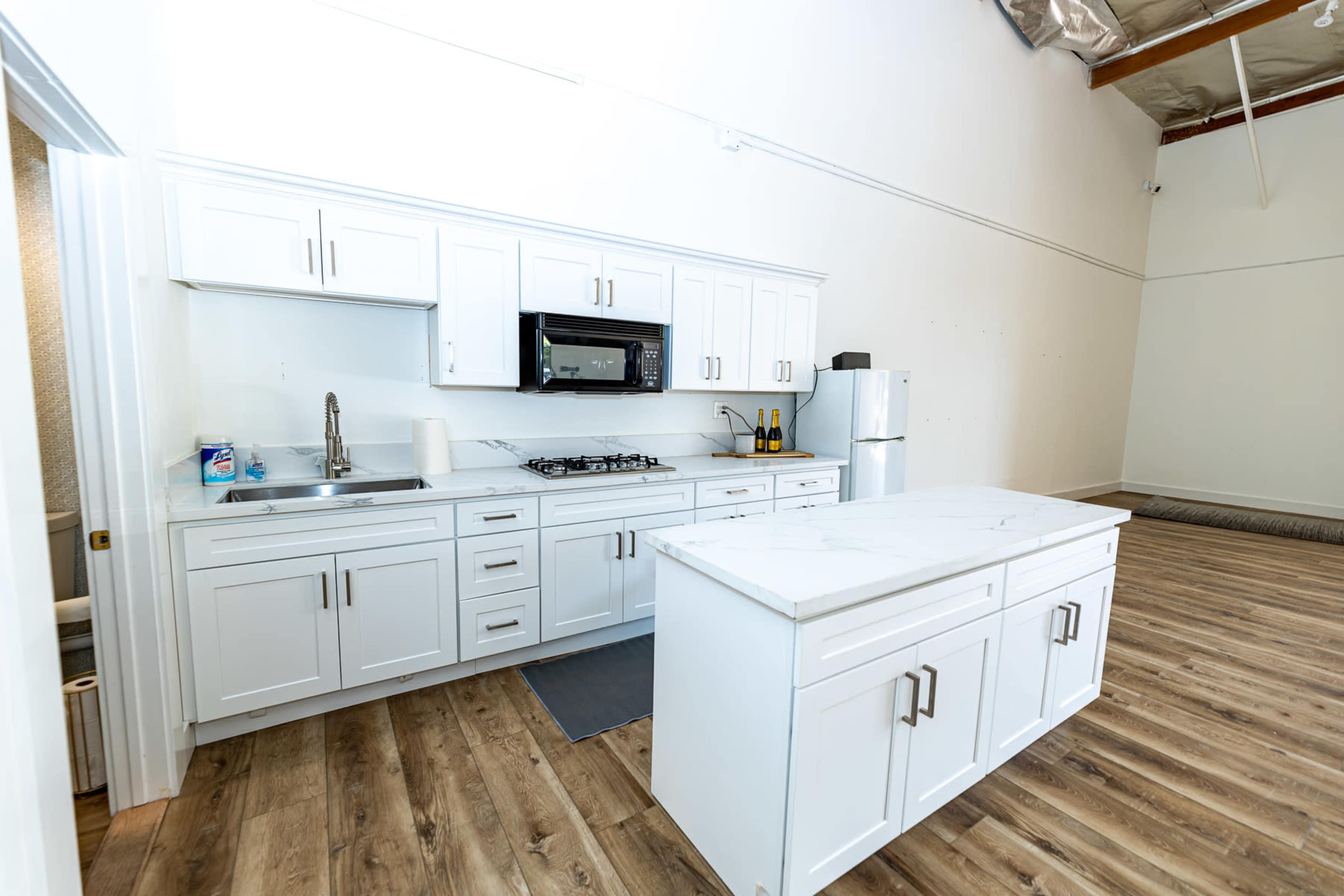 A modern kitchen with white cabinets, a marble countertop island, and stainless steel appliances in a spacious area with wooden flooring.