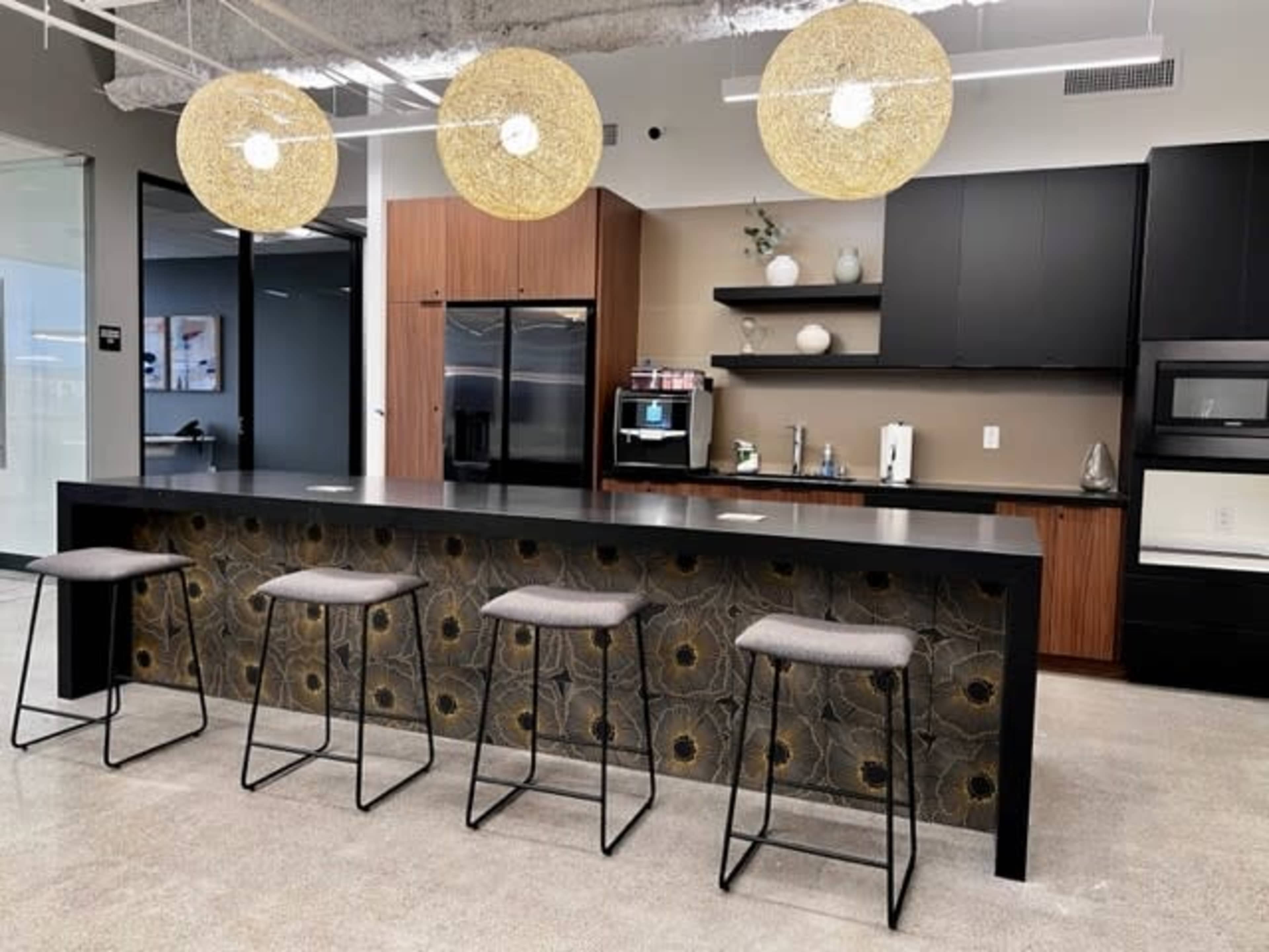 A modern kitchen area featuring a dark countertop, a row of gray bar stools, and unique pendant lights hanging above.