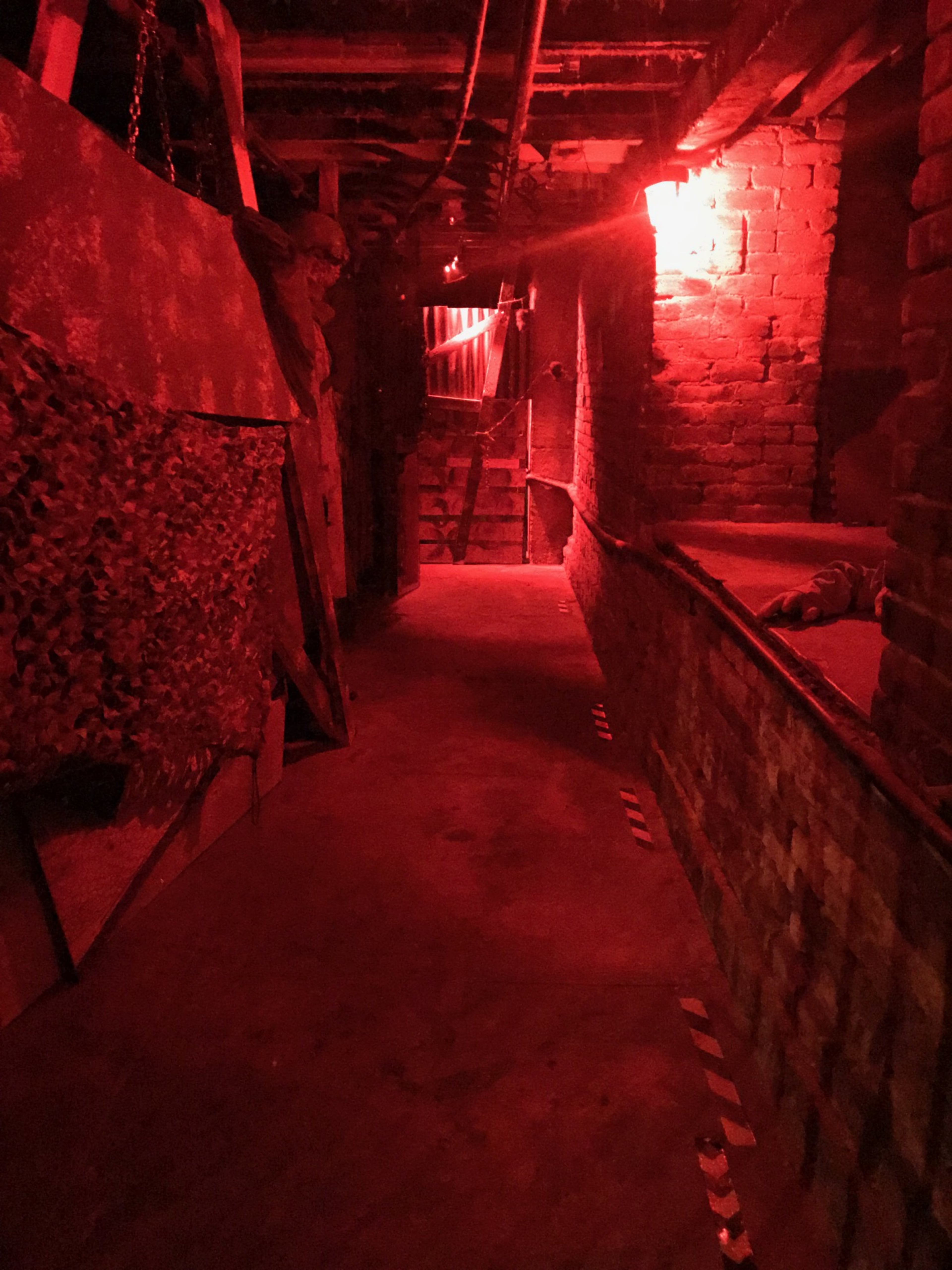 The dimly lit corridor features red lighting, exposed brick walls, and various construction materials along the sides.