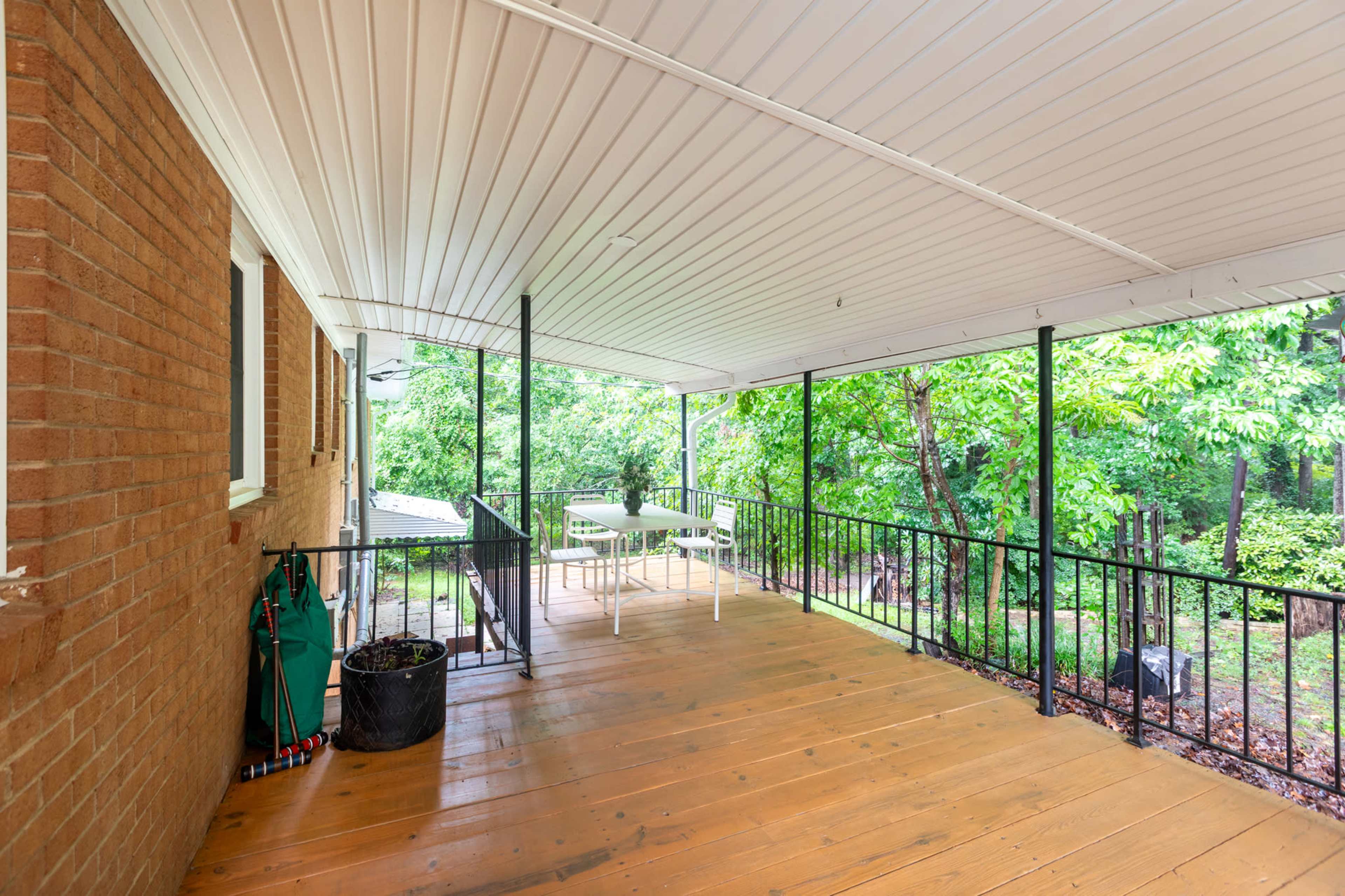 The image shows a covered wooden patio with a table and chairs overlooking a lush green yard.
