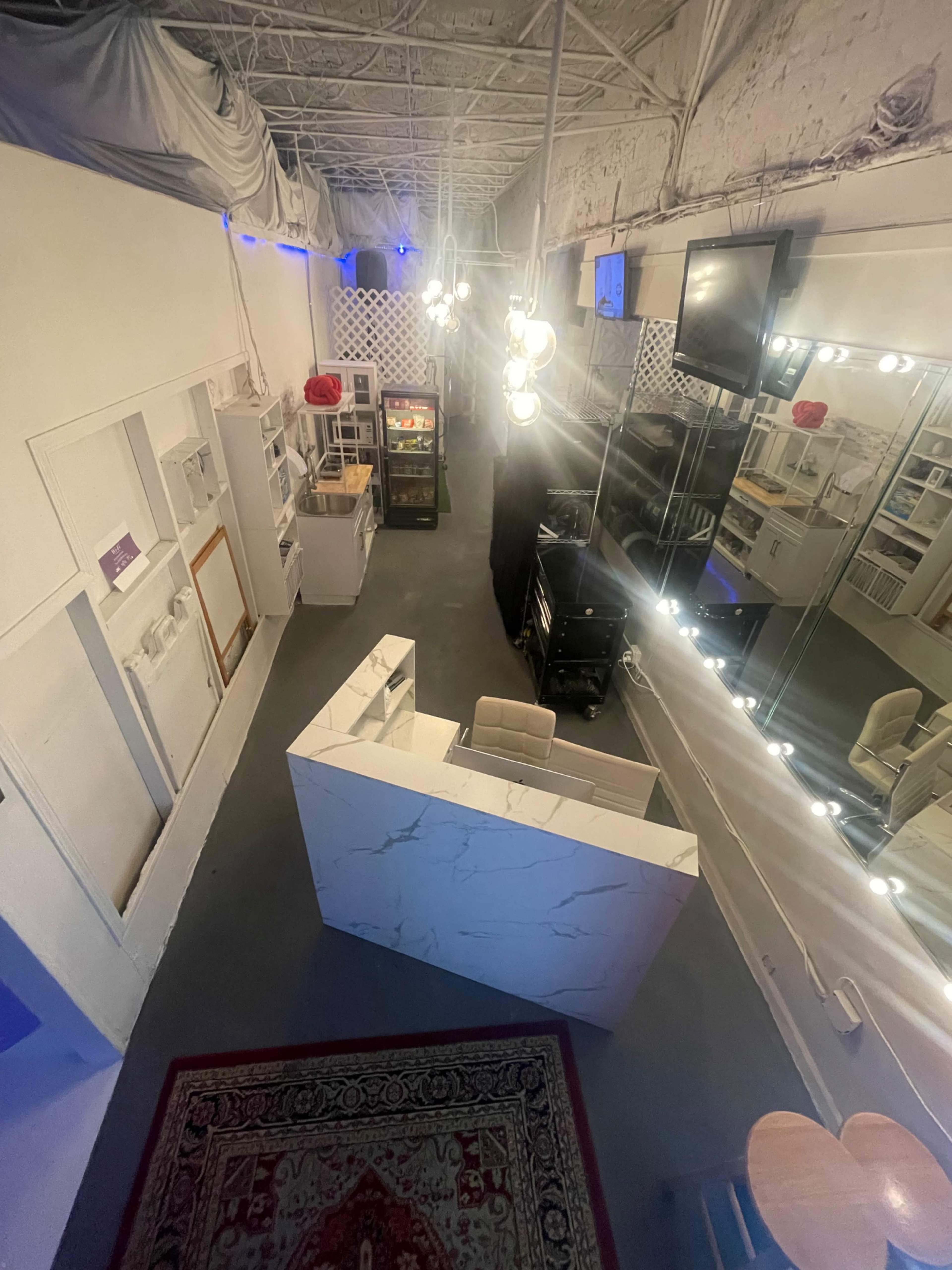 The image shows a modern interior space with a reception desk, mirrored wall, and various furniture pieces, illuminated by pendant lights.