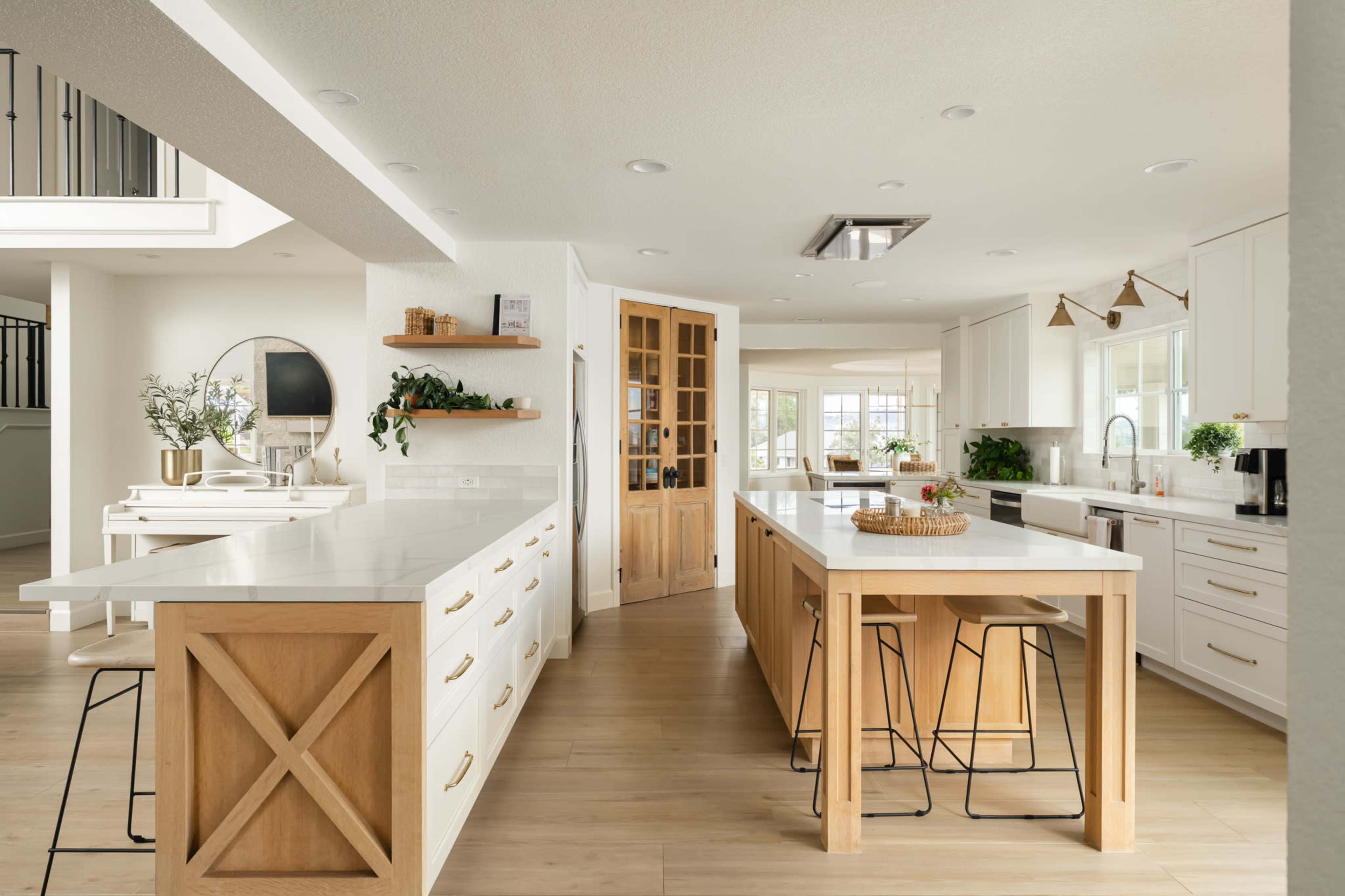 The image shows a modern kitchen with light-colored cabinetry, a large central island with white countertops, and wooden accents, all complemented by natural light.