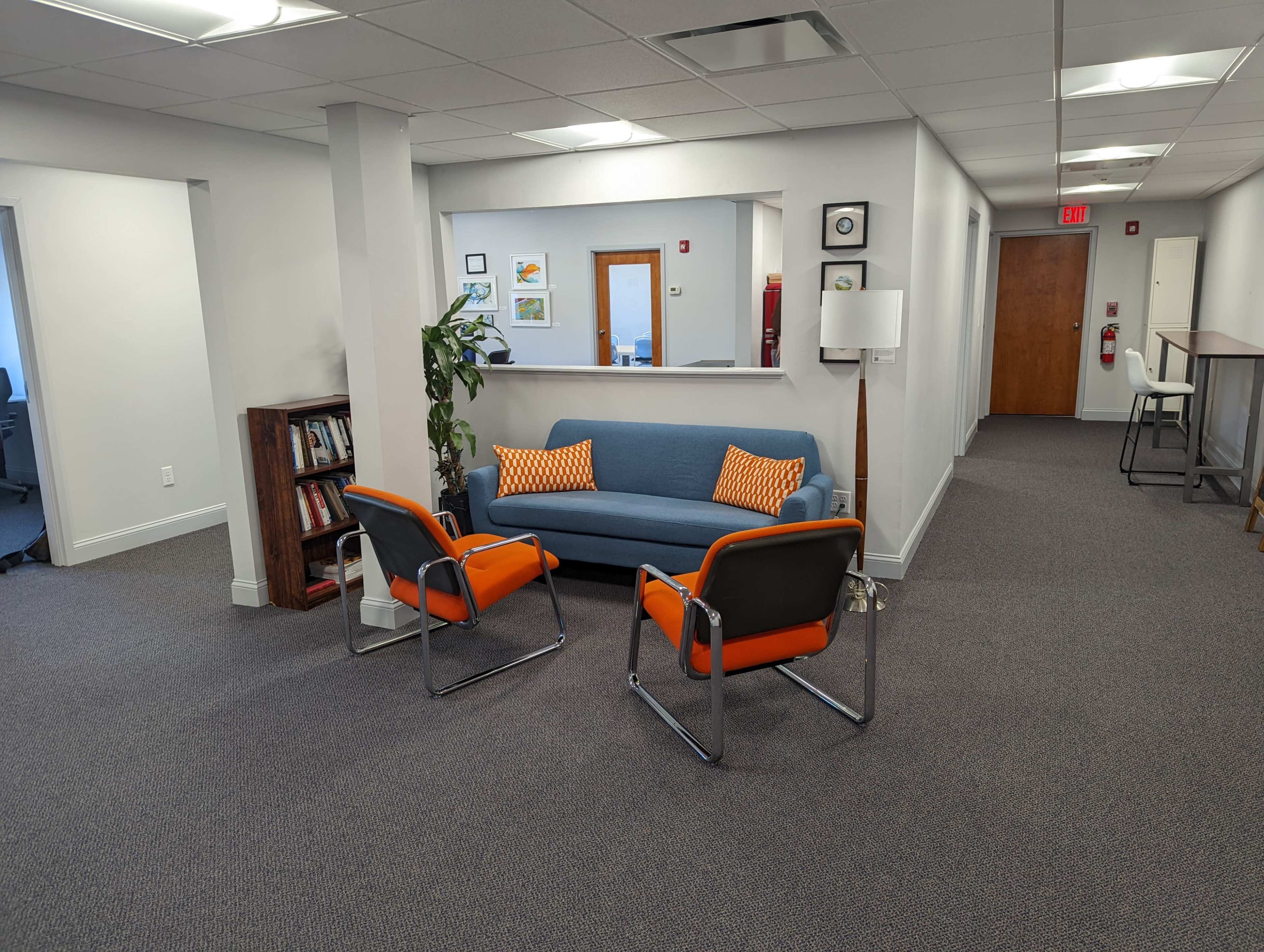 A modern office lobby with a blue couch and two orange-accented chairs arranged around a small table.