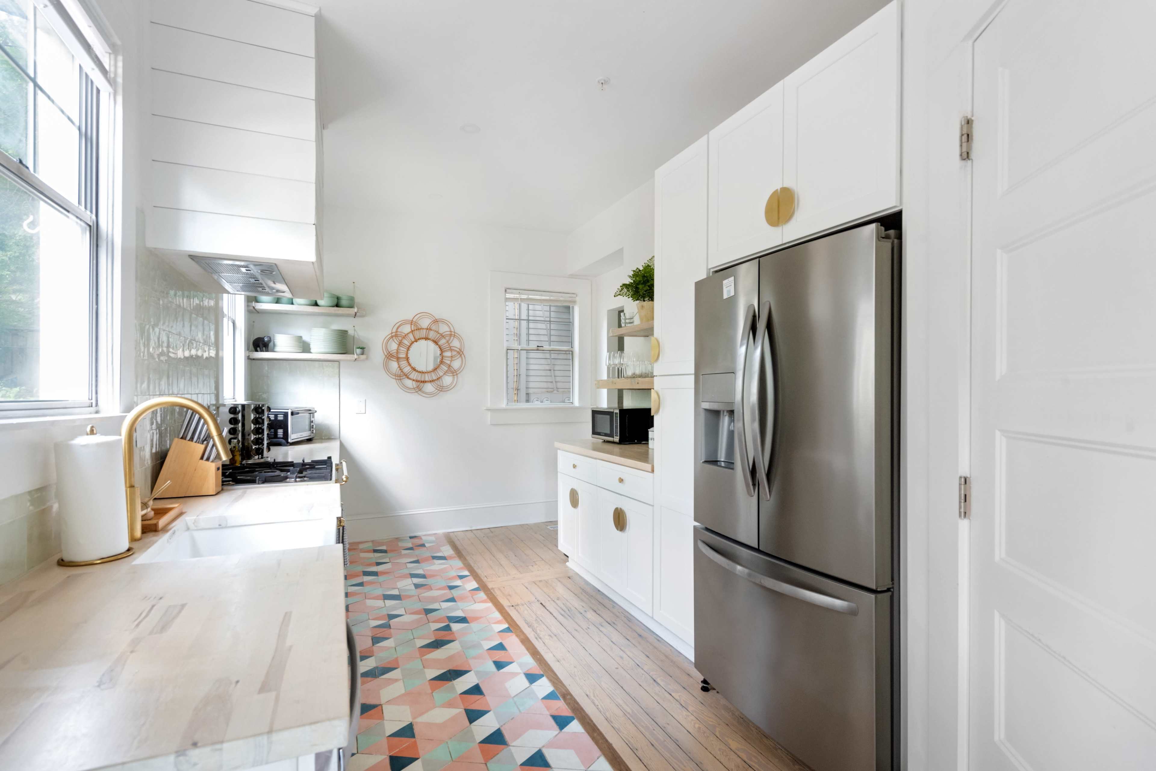 The image shows a modern kitchen with white cabinetry, a stainless steel refrigerator, and a geometric patterned floor.
