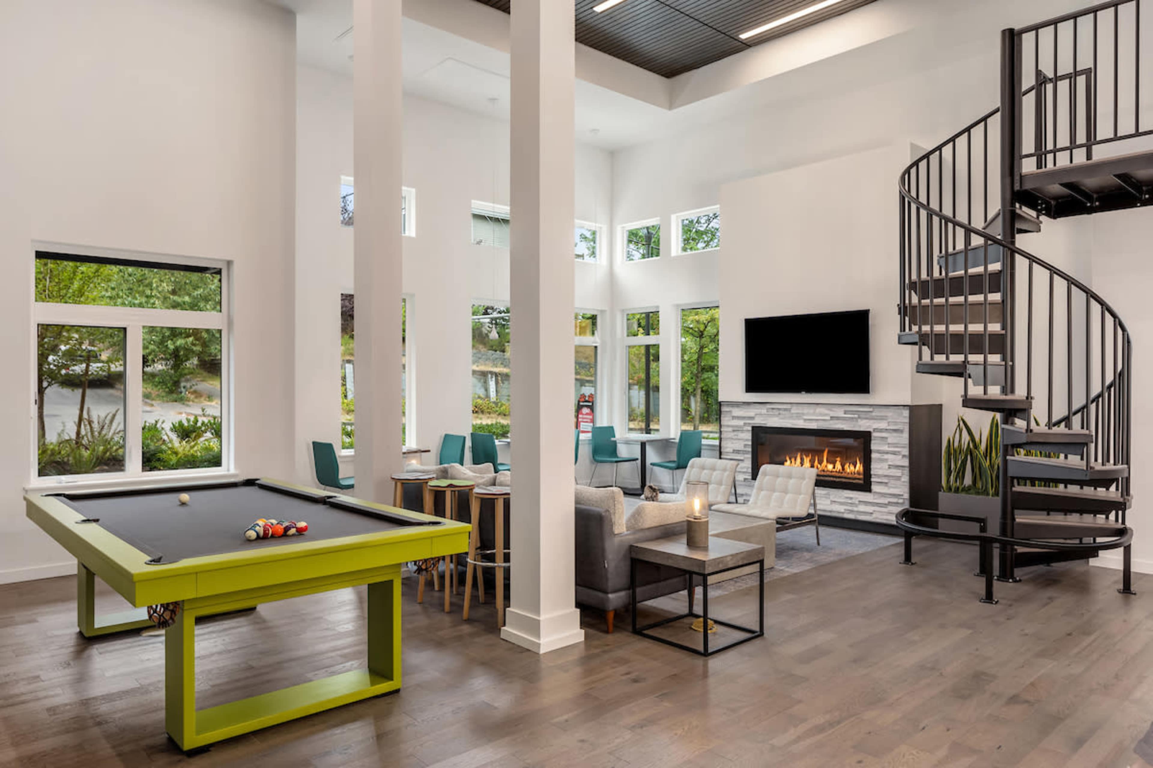 A modern common area featuring a pool table, spiral staircase, a fireplace, and large windows that allow natural light to fill the space.