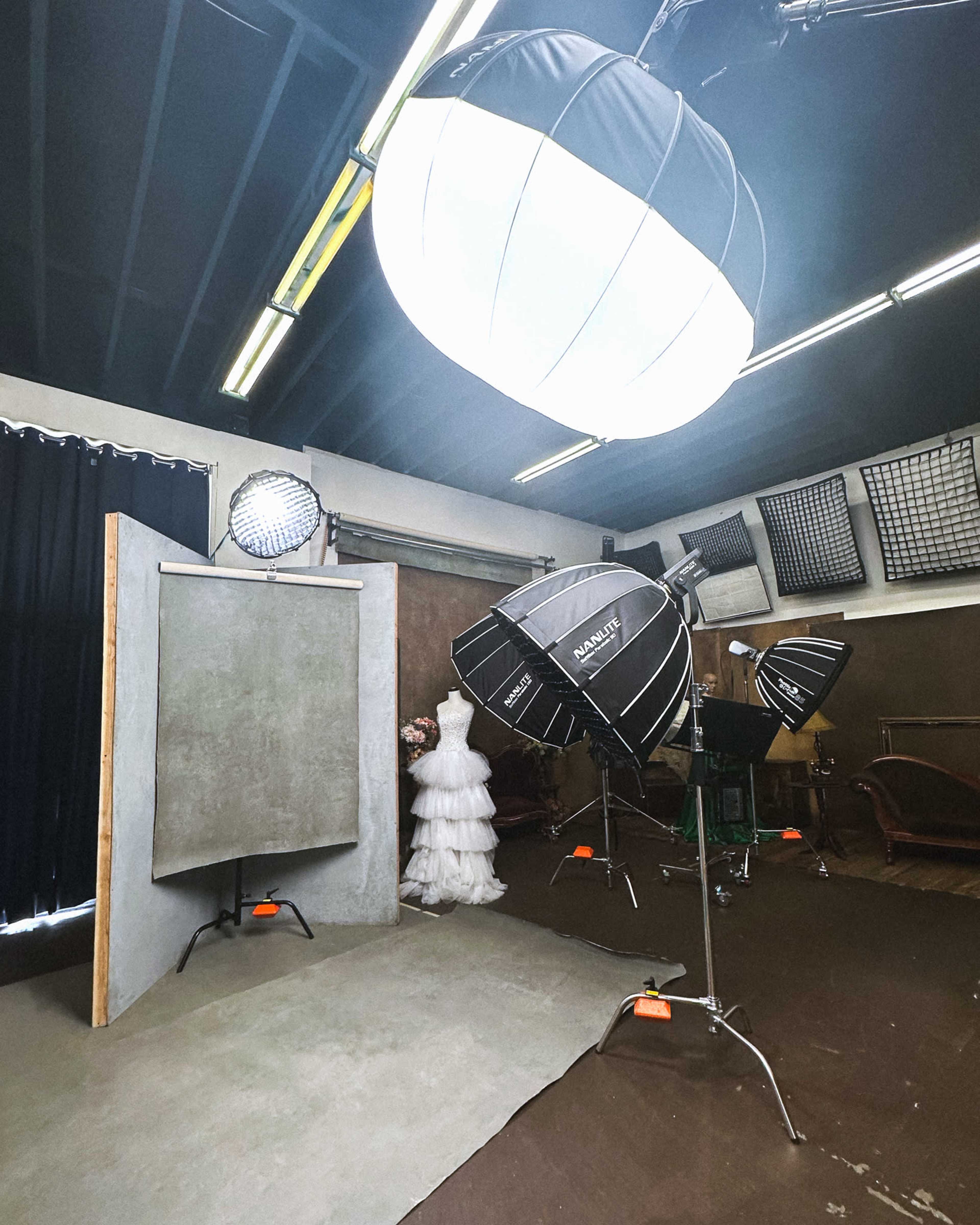 The image shows a photography studio setup featuring a mannequin dressed in a white gown, surrounded by various lighting equipment and a backdrop.