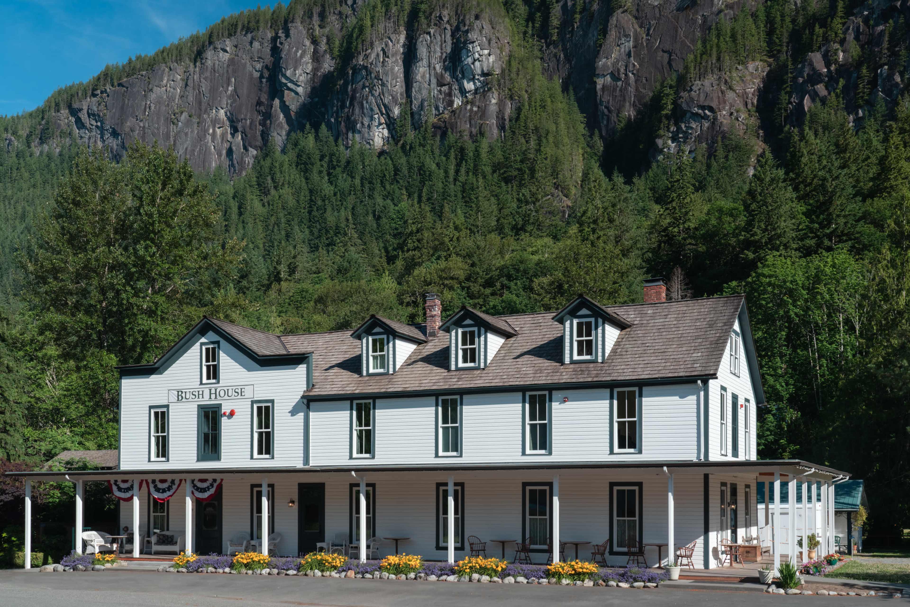 A large, two-story building labeled "Bush House" set against a backdrop of a steep, forested mountain.