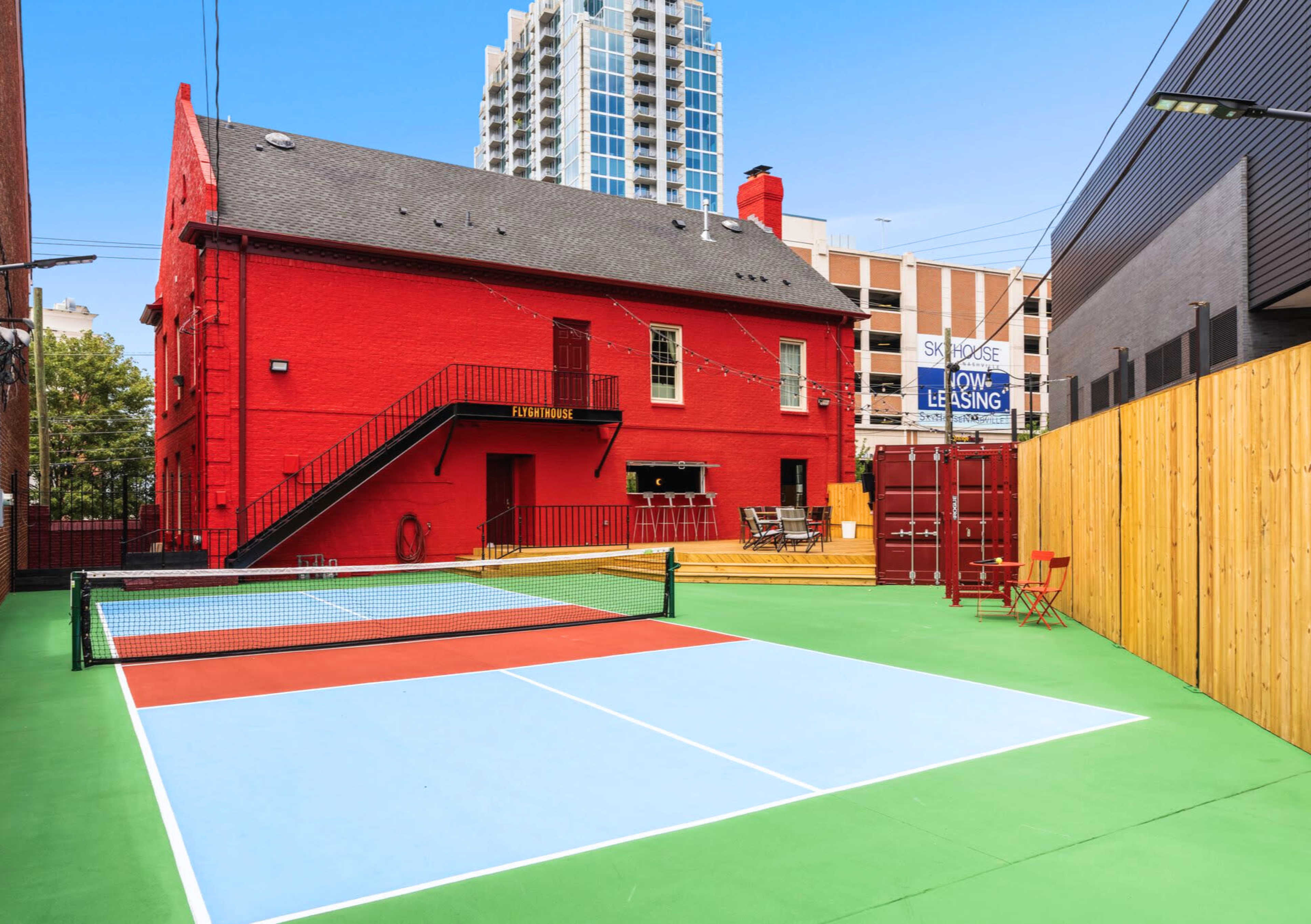 The image shows a vibrant red building alongside two tennis courts with blue and orange surfaces.