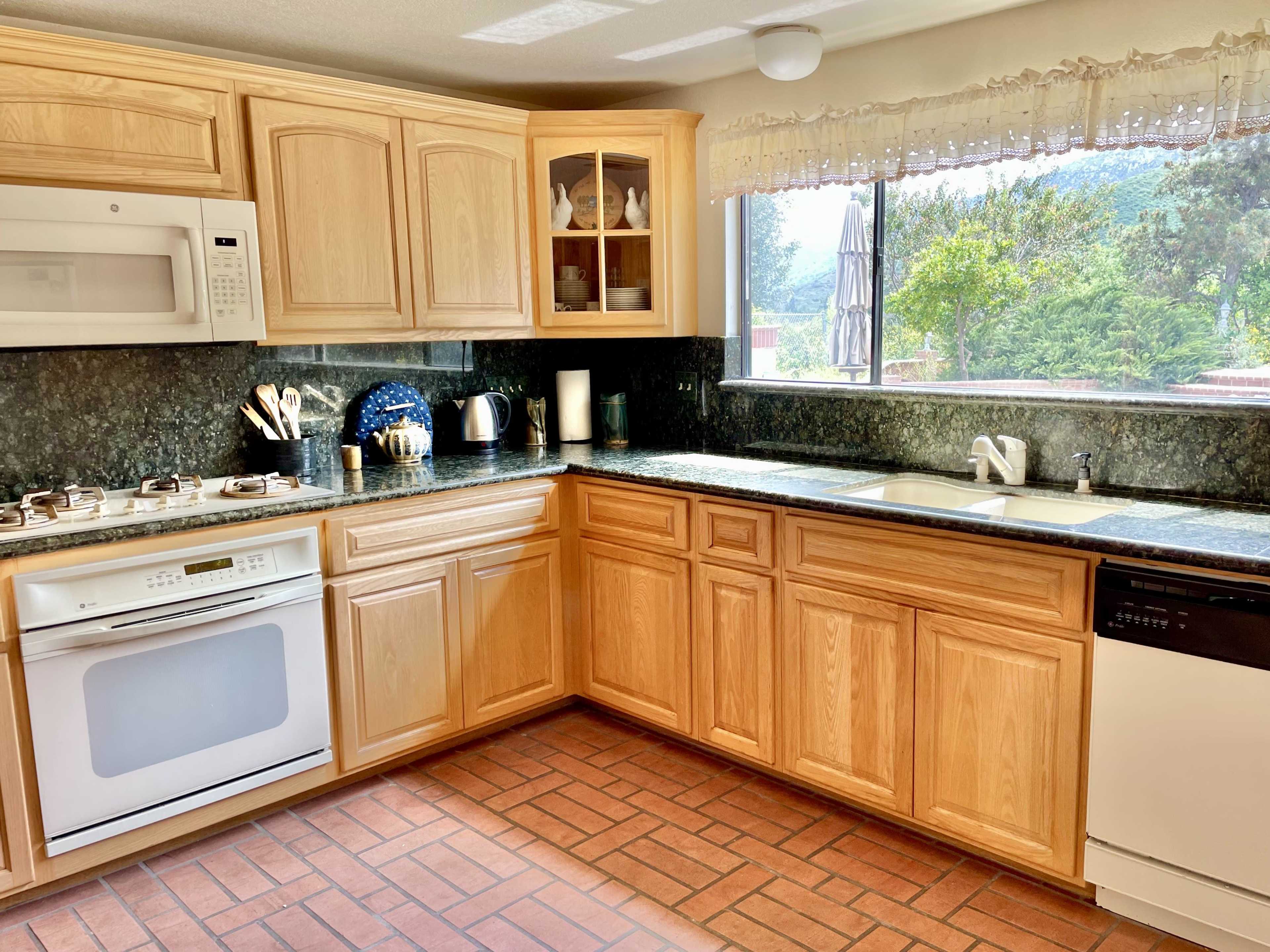 A modern kitchen features wooden cabinets, a granite countertop, and a window overlooking greenery.