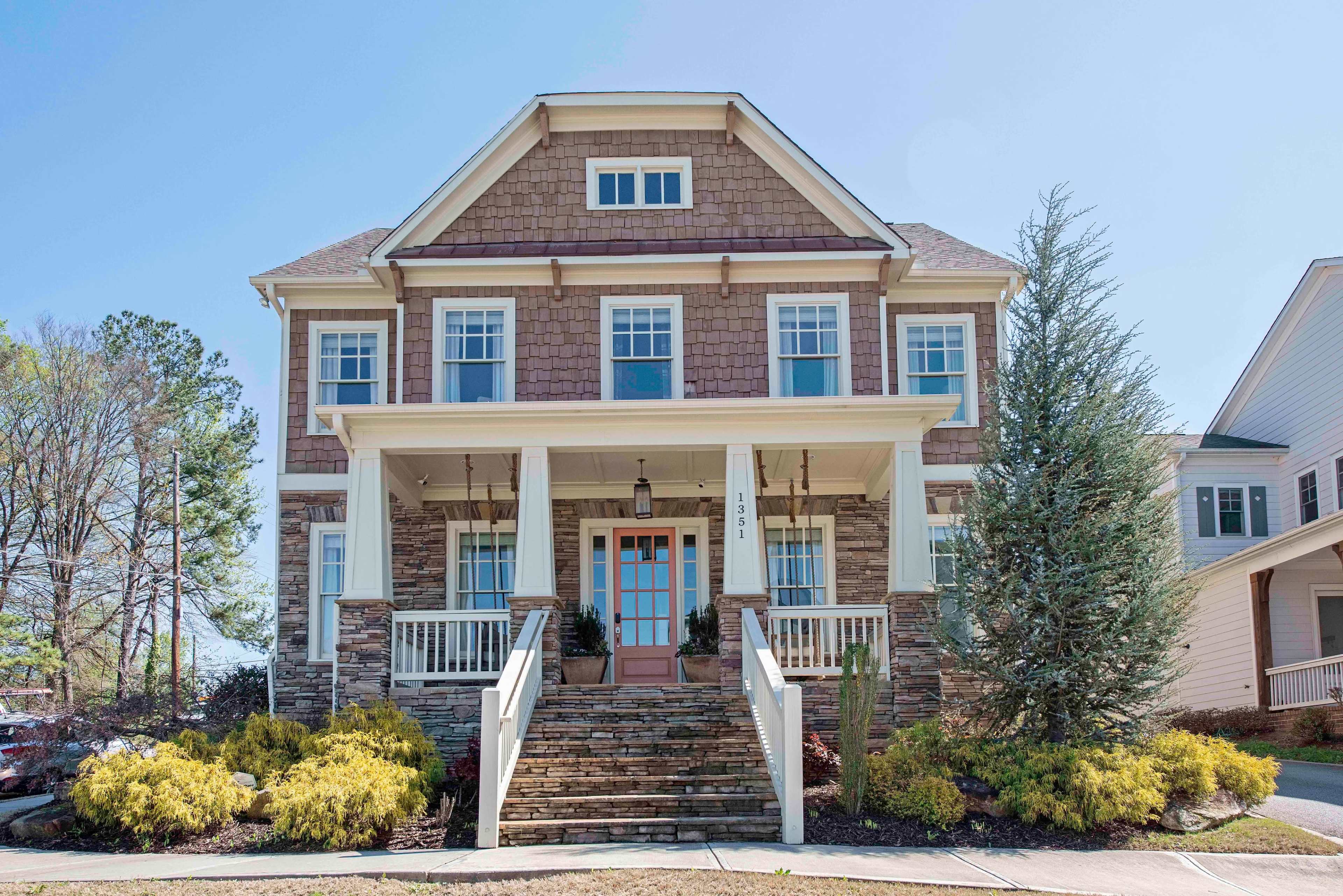 A large two-story house features a combination of stone and wood siding with a front porch and landscaped yard.