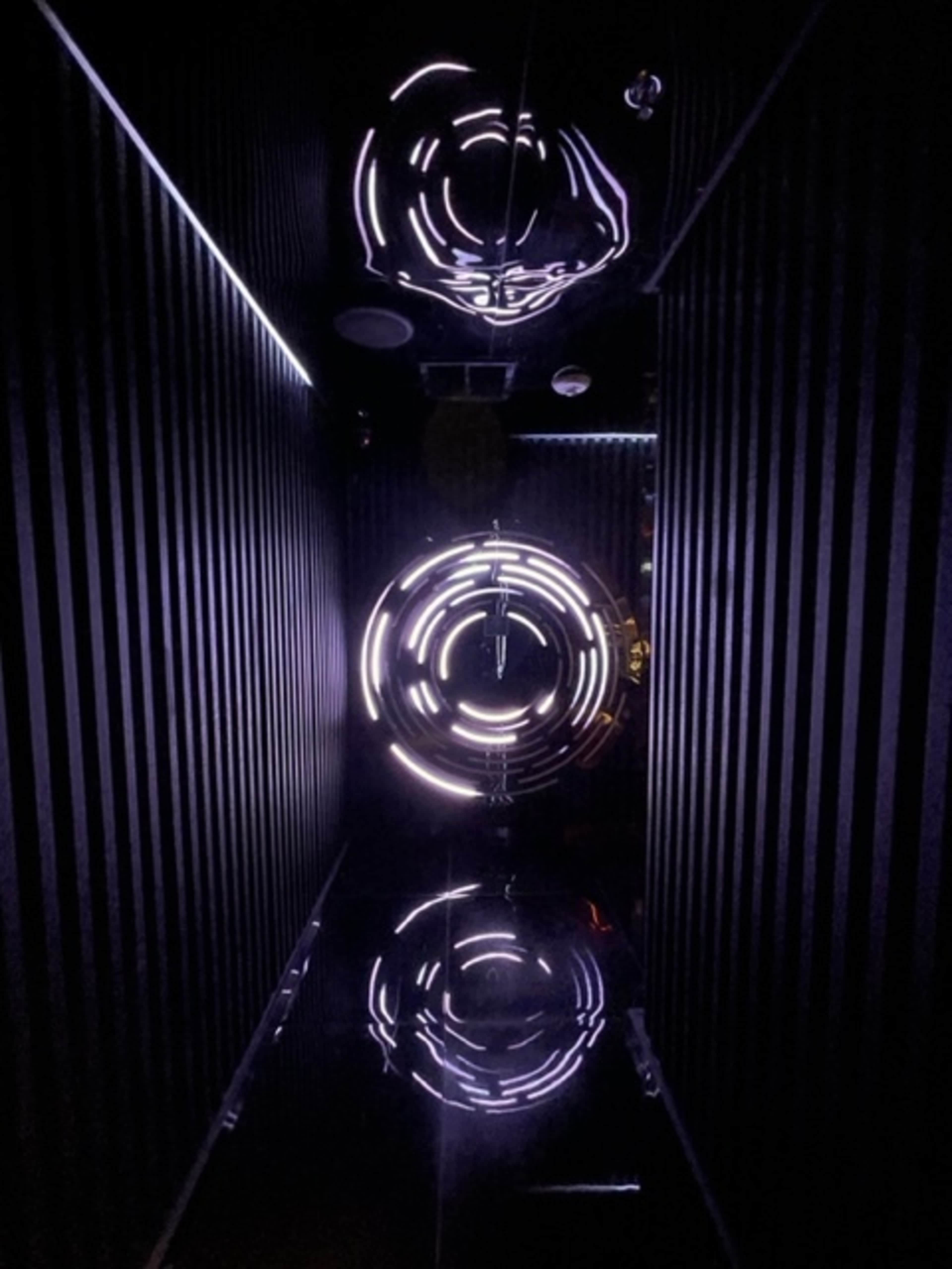 A narrow, dark hallway featuring circular lights reflected on glossy surfaces.