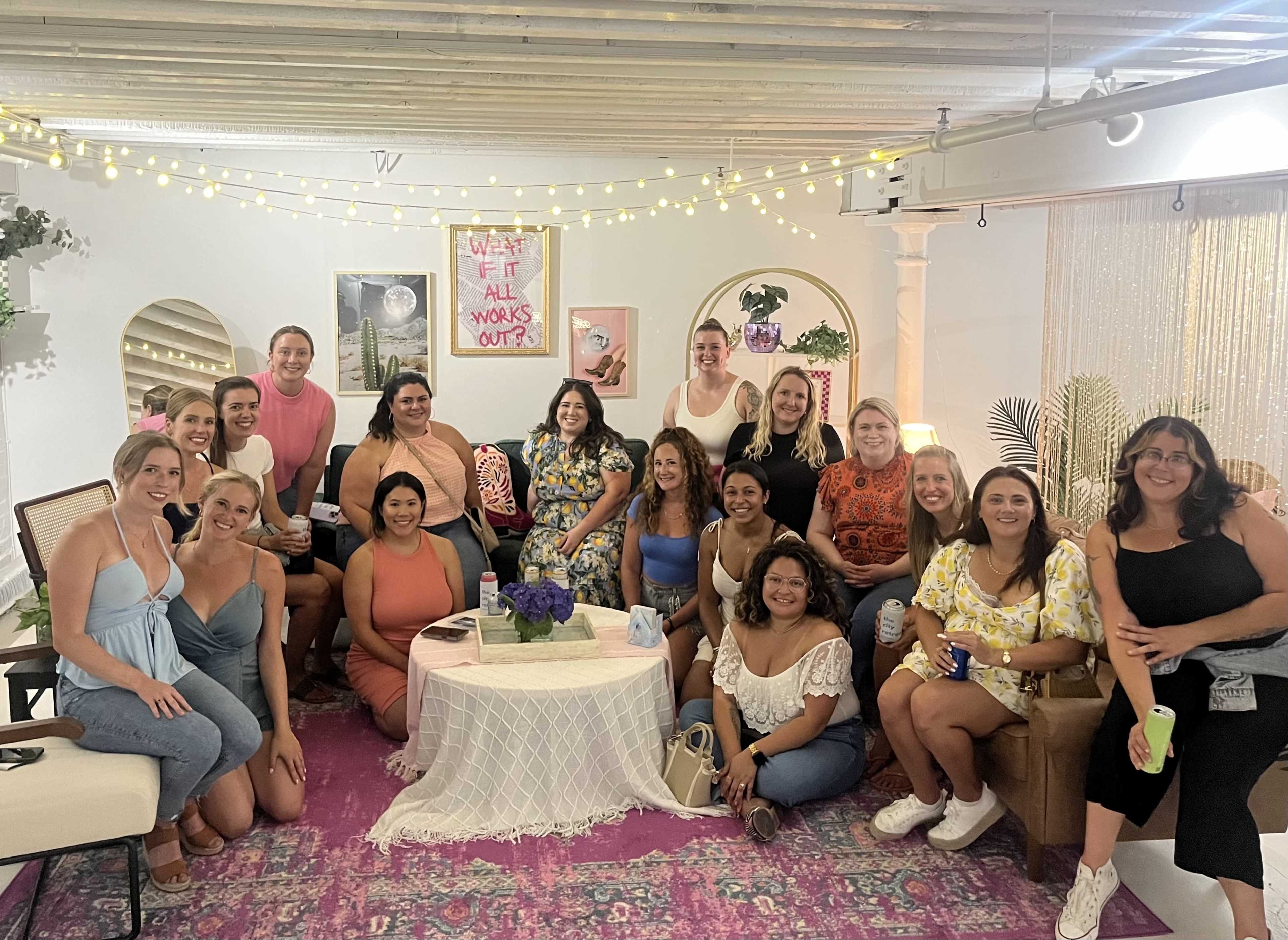 A group of diverse individuals poses together in a stylishly decorated room with string lights and colorful furnishings.