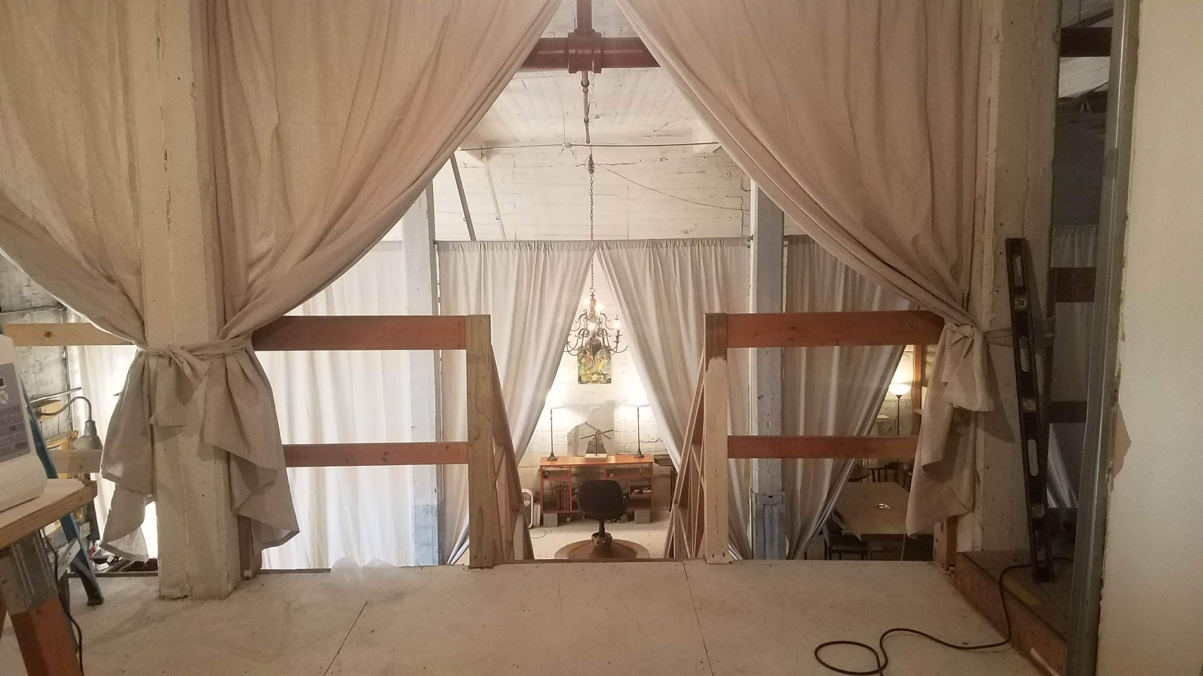 A wooden railing leading to a spacious room with white curtains, a chandelier, and furniture visible in the background.
