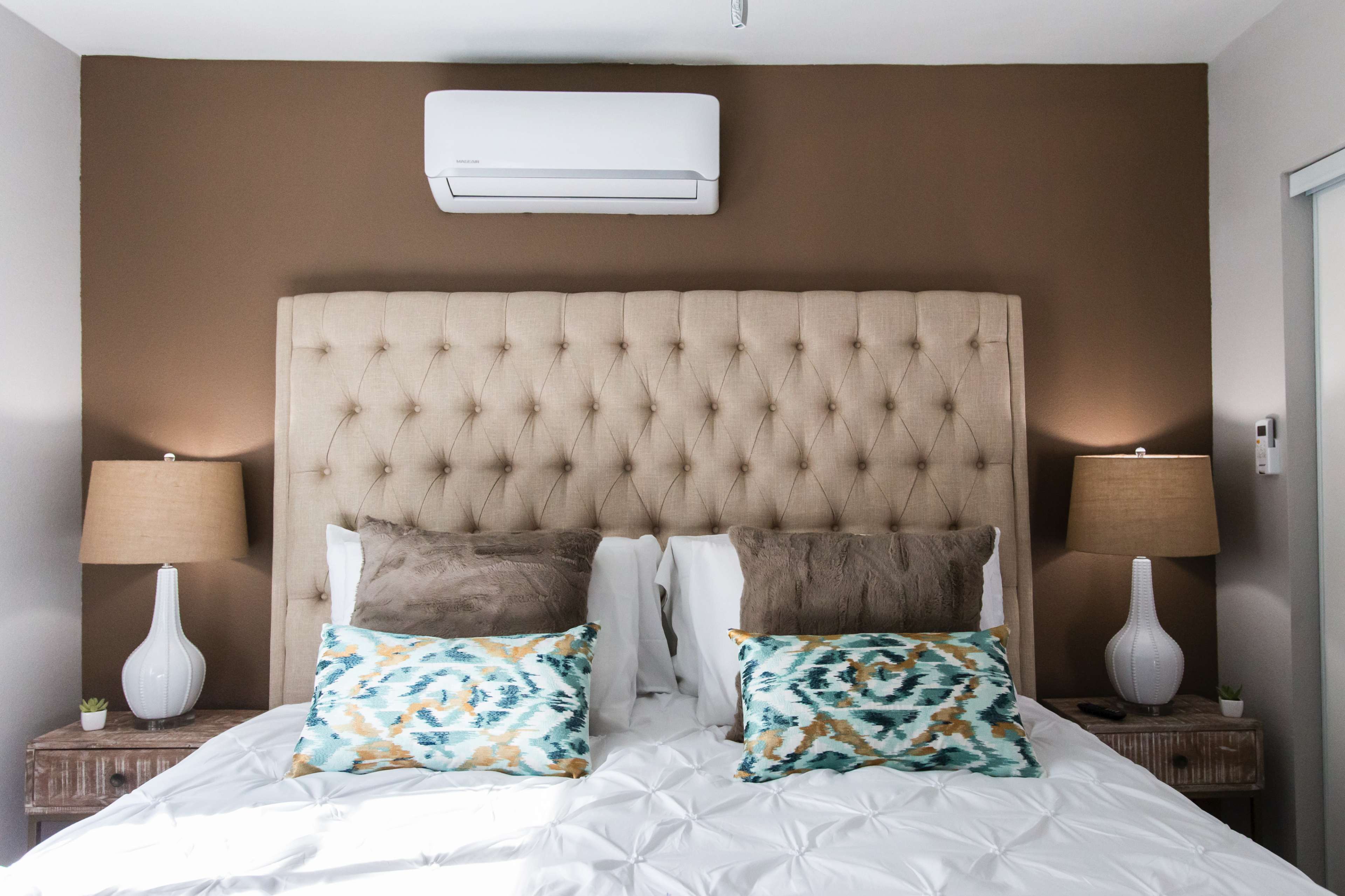 A well-appointed bedroom features a tufted beige headboard, two decorative pillows, and matching bedside lamps on wooden nightstands.
