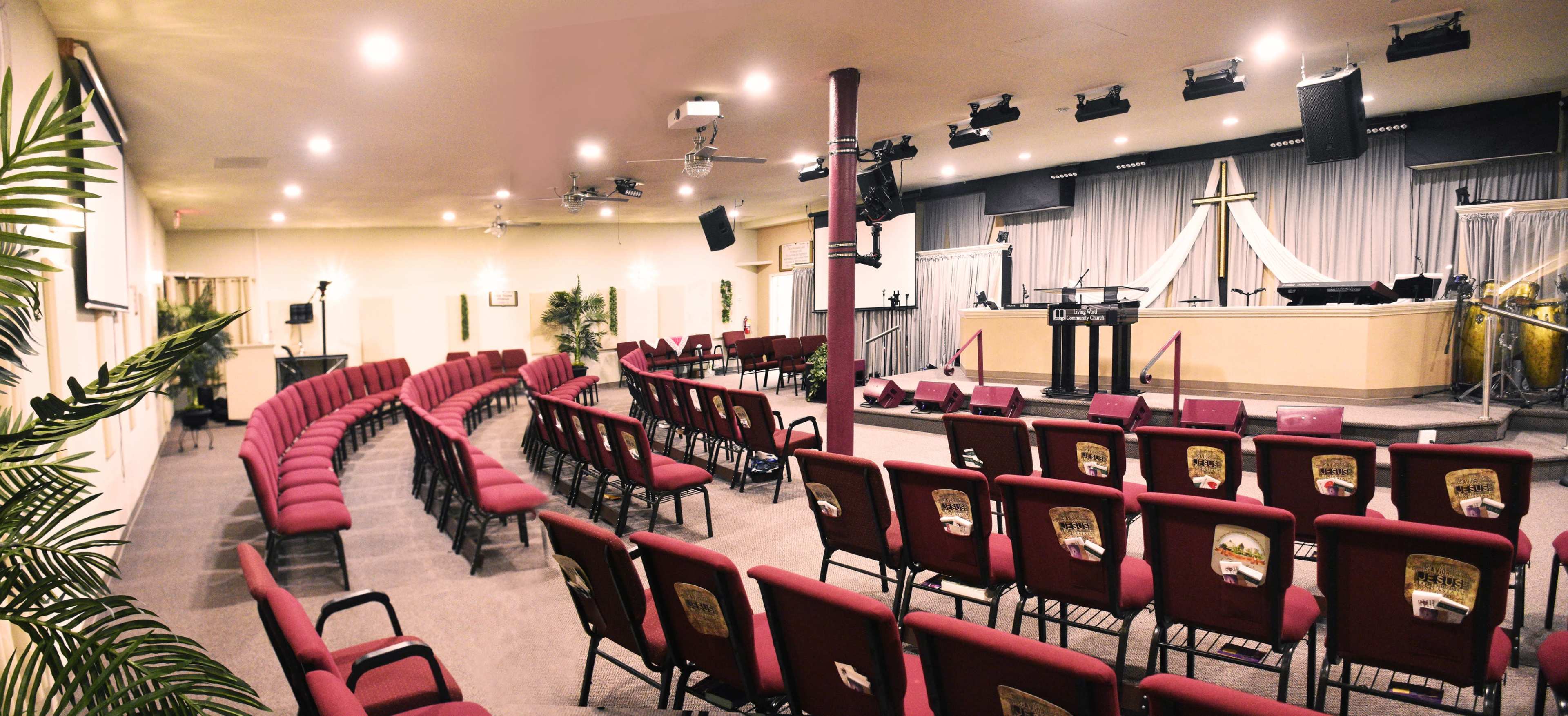 A church interior with red chairs arranged in a semicircular layout facing a stage.