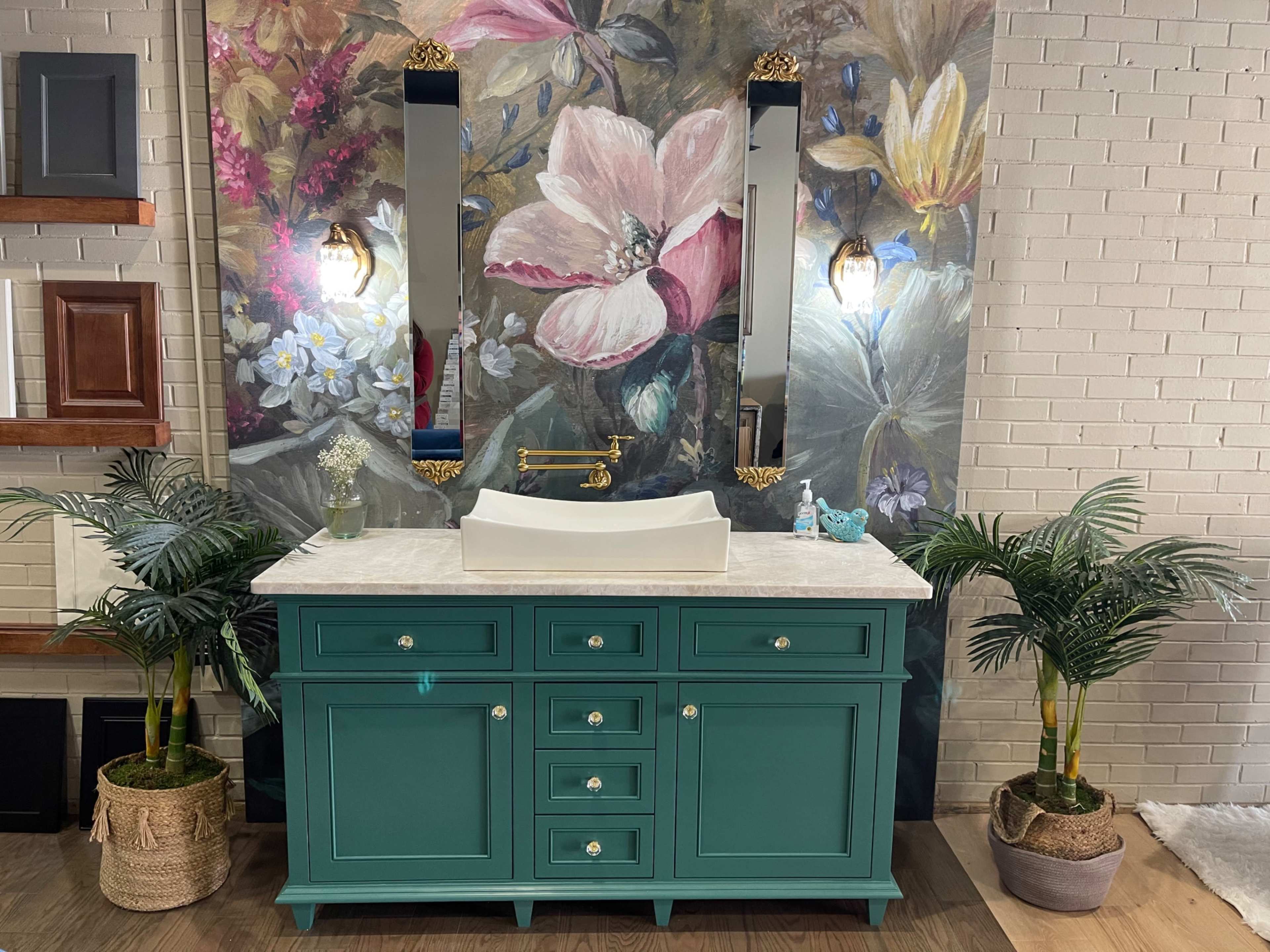 A turquoise bathroom vanity with a white countertop and a rectangular sink is set against a floral mural, flanked by two mirrors and surrounded by potted plants.