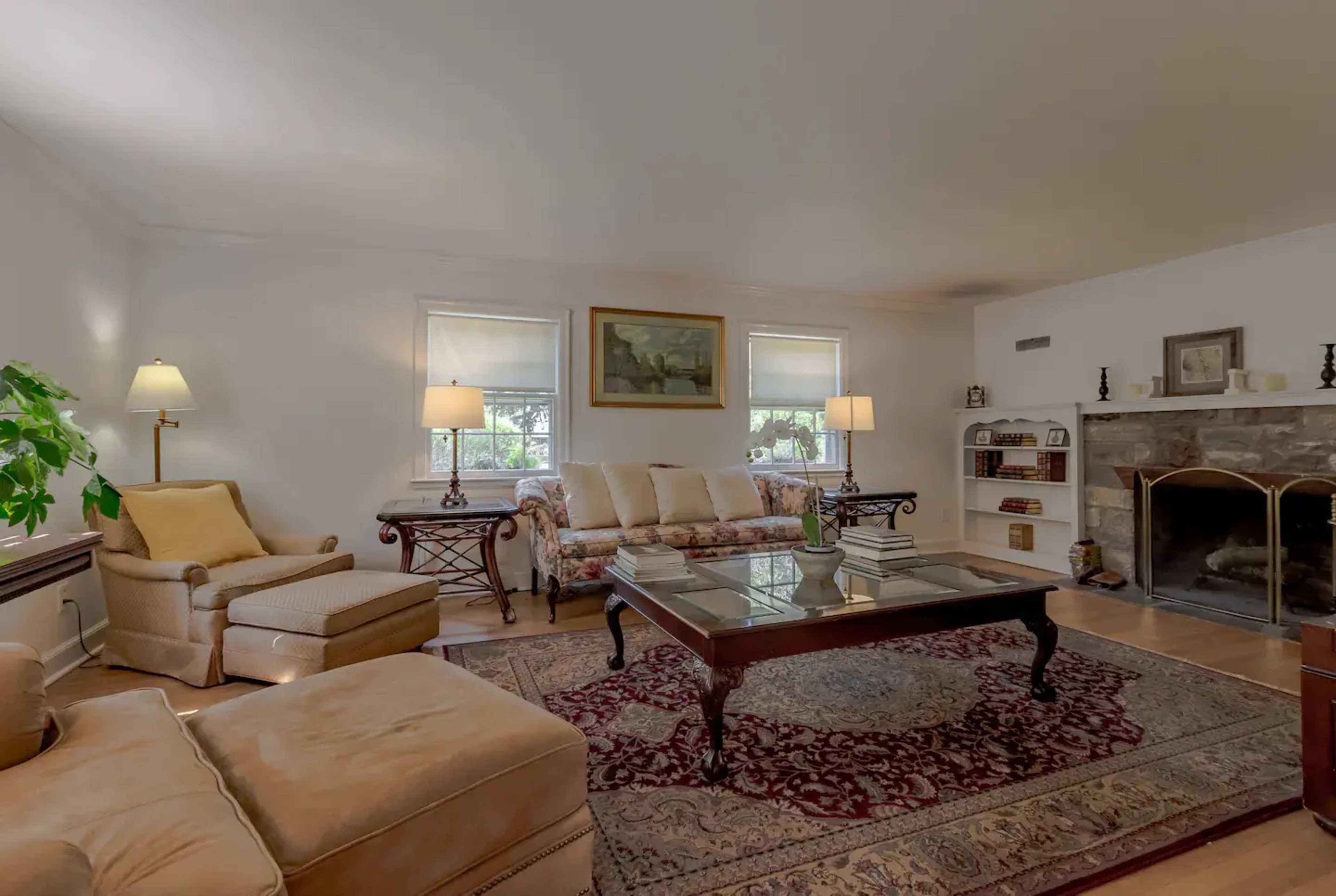 The living room features a cream-colored sofa and an armchair, a wooden coffee table, a stone fireplace, and light-colored walls with framed artwork.