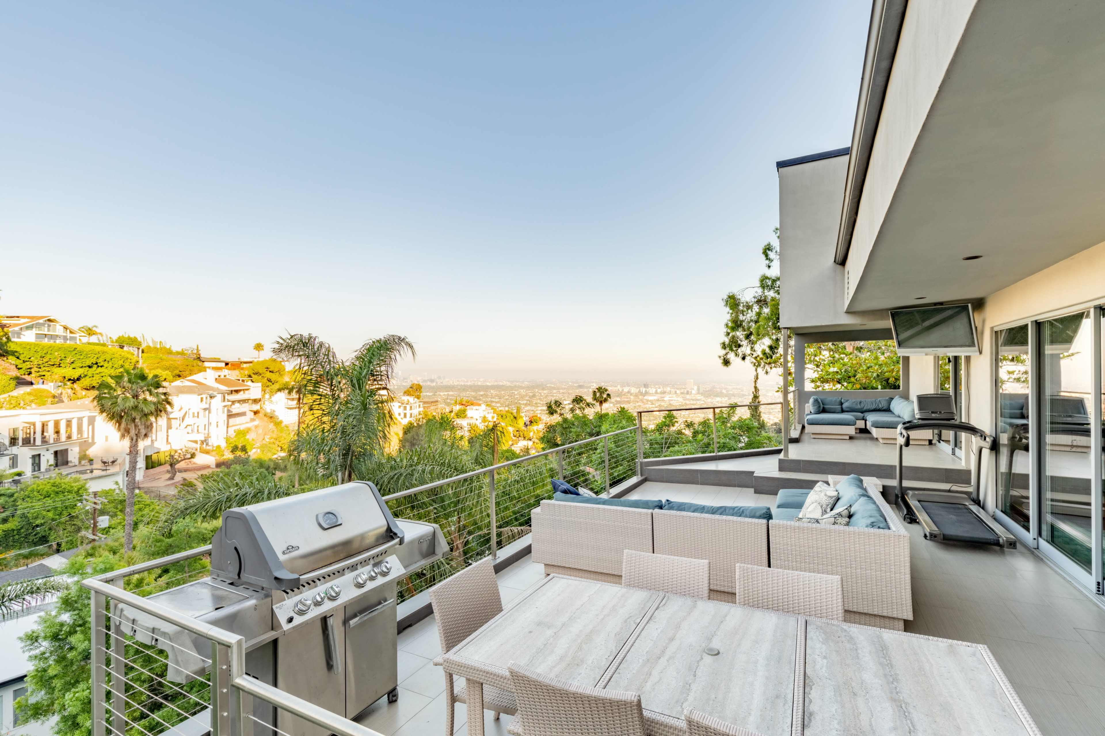 A modern outdoor patio with a grill and a dining area, overlooking a cityscape in the background.