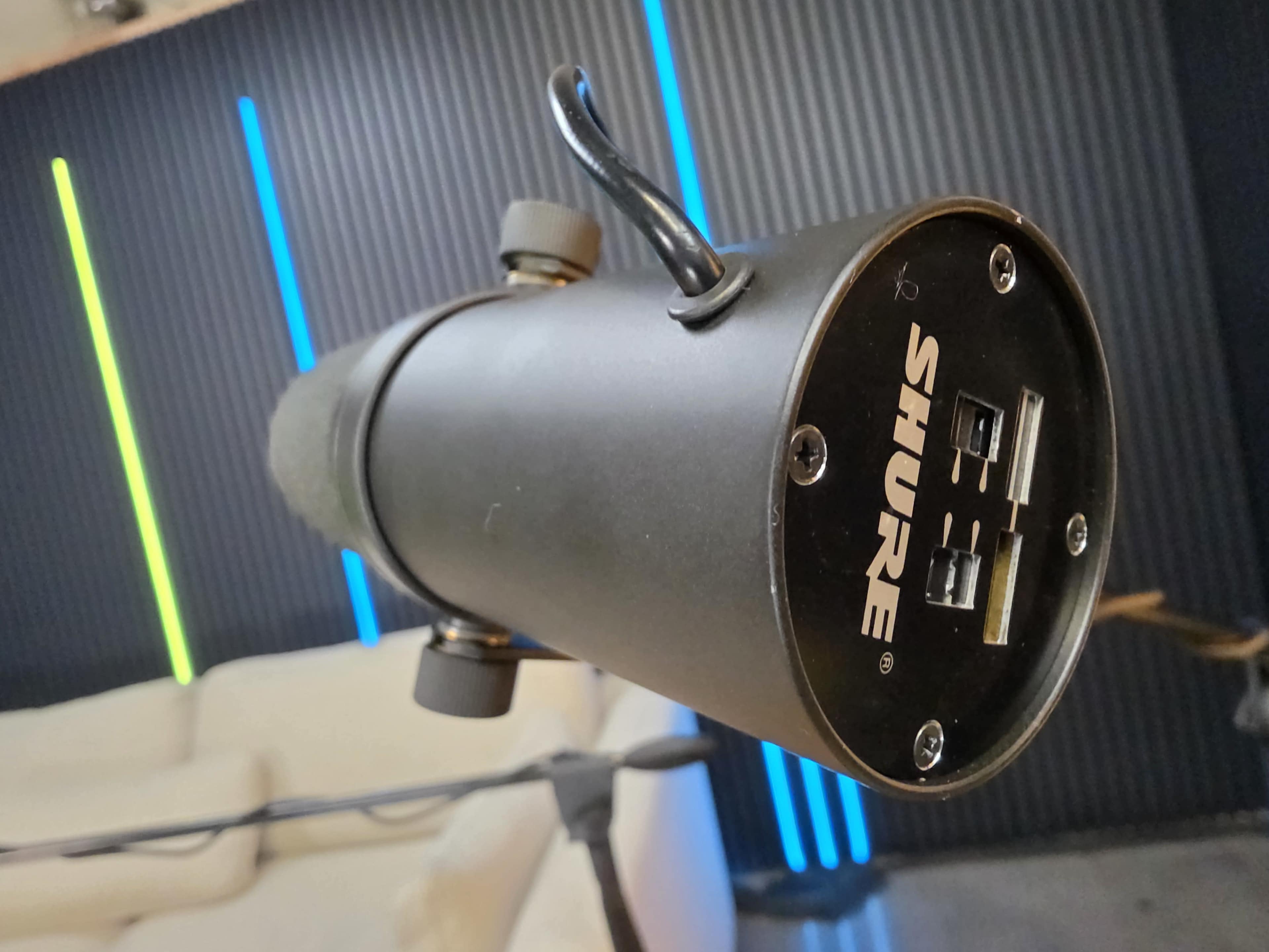A close-up view of the back of a Shure microphone, showcasing its USB connections and mounting hardware against a backdrop of colorful vertical lights.