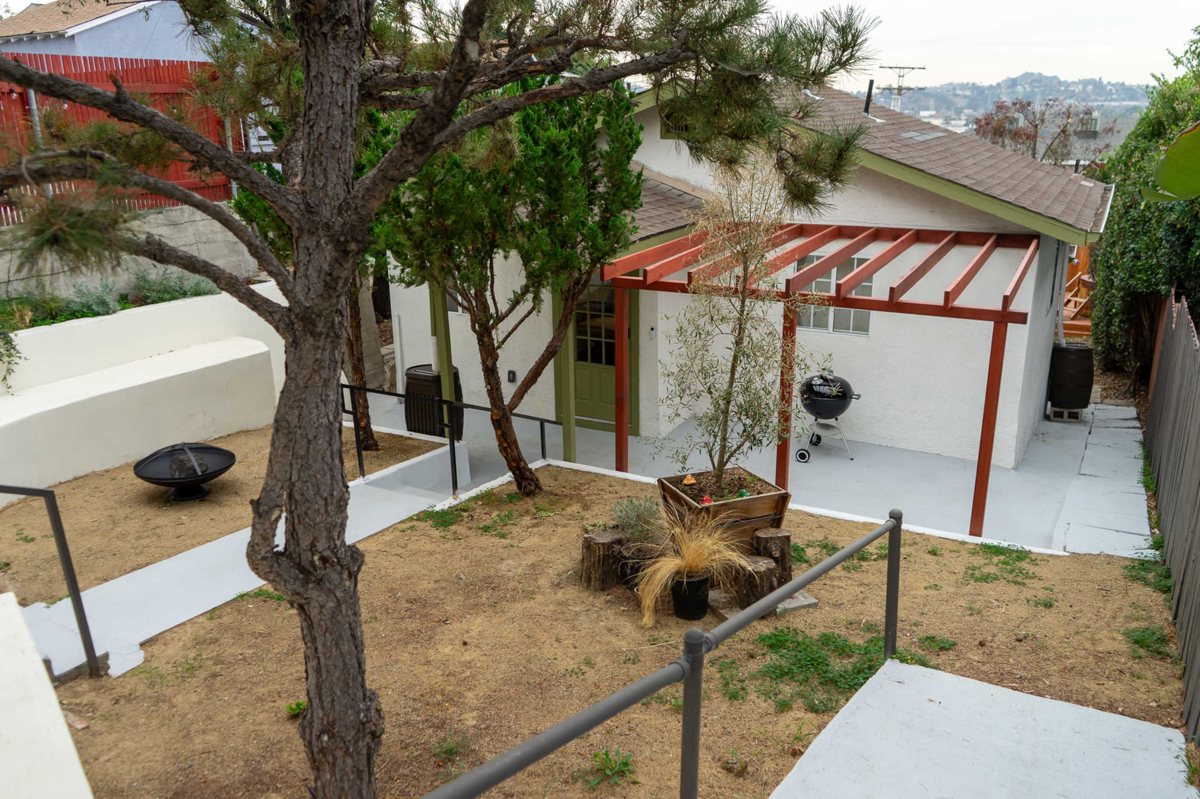 A single-story house with a red accent overhang, surrounded by a sloped yard and a wooden railing.
