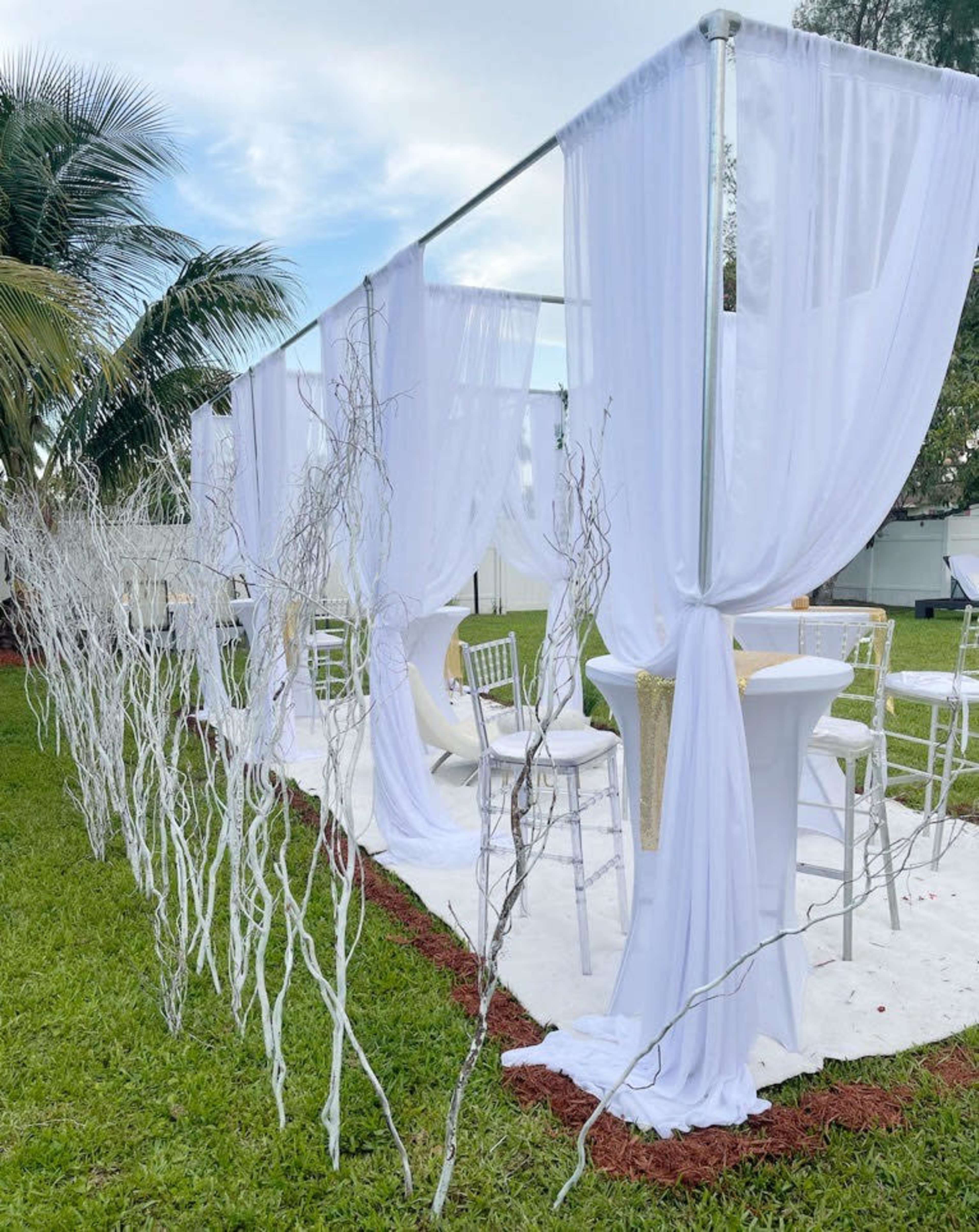 A white tent with sheer curtains is set up outside on a grassy area, surrounded by bare twigs arranged decoratively.