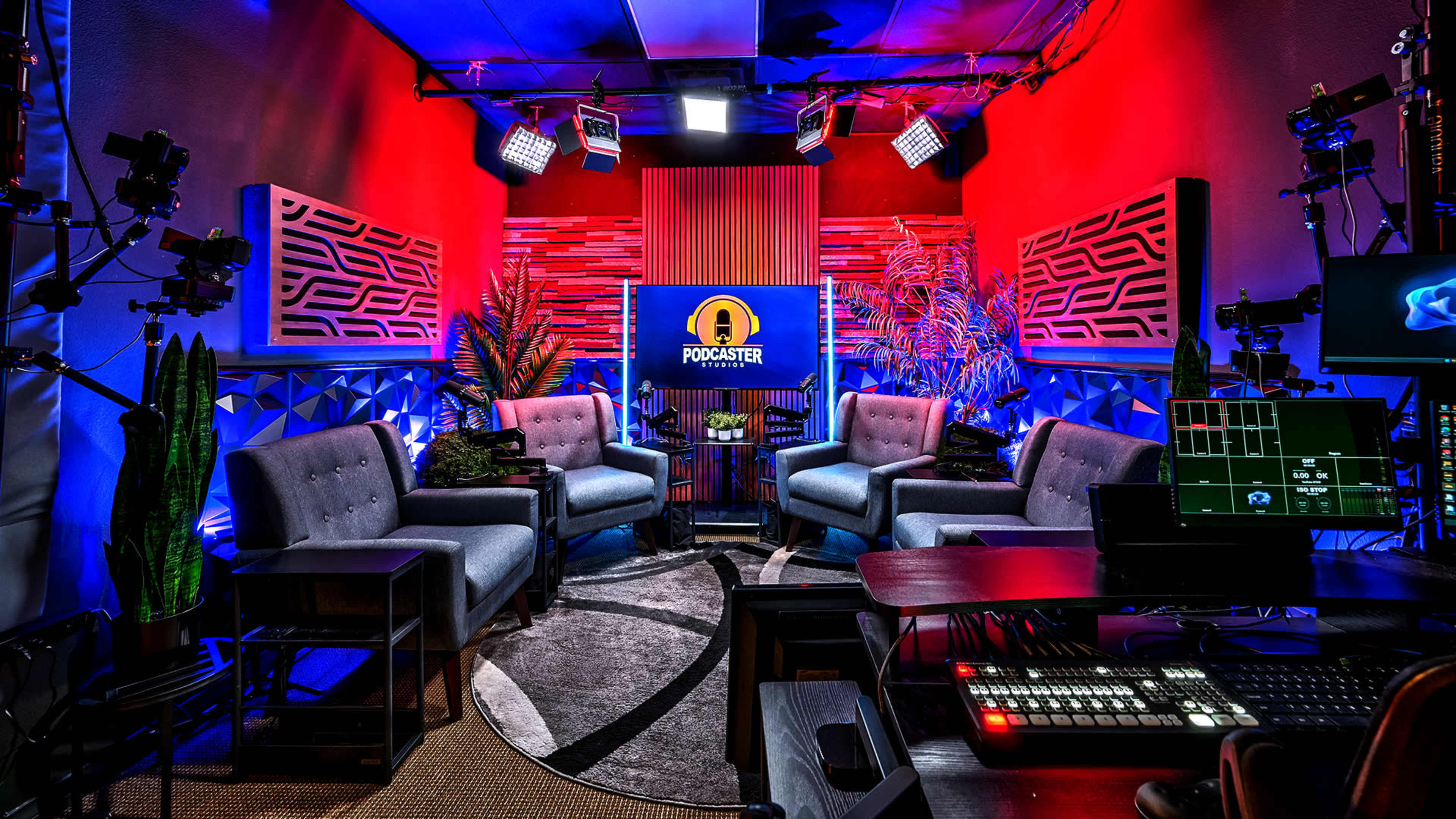 The image shows a modern podcasting studio with gray couches arranged around a circular rug, colorful lights illuminating the space, and equipment set up for recording.