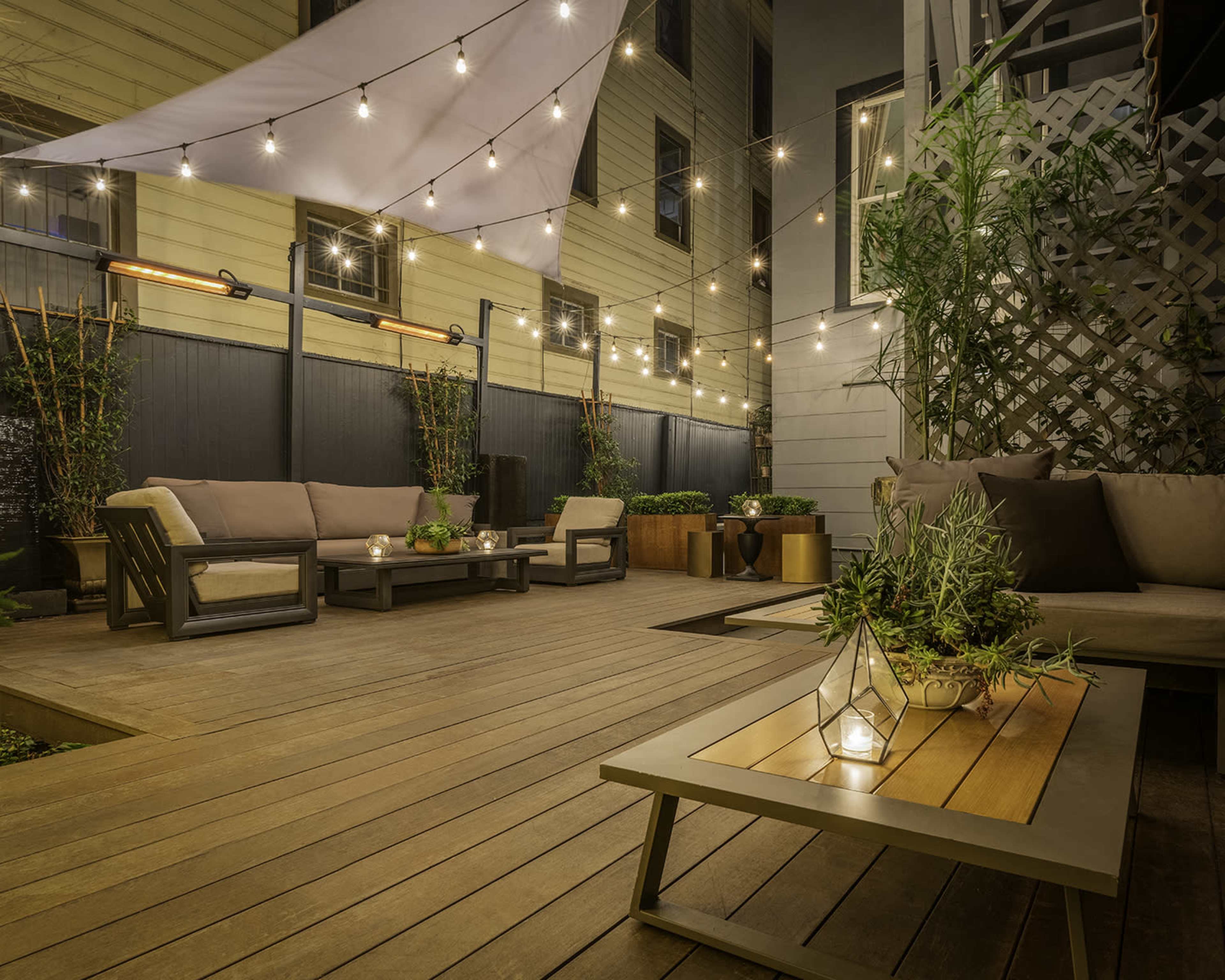 The image shows a cozy outdoor patio area with string lights overhead, featuring modern seating and potted plants.