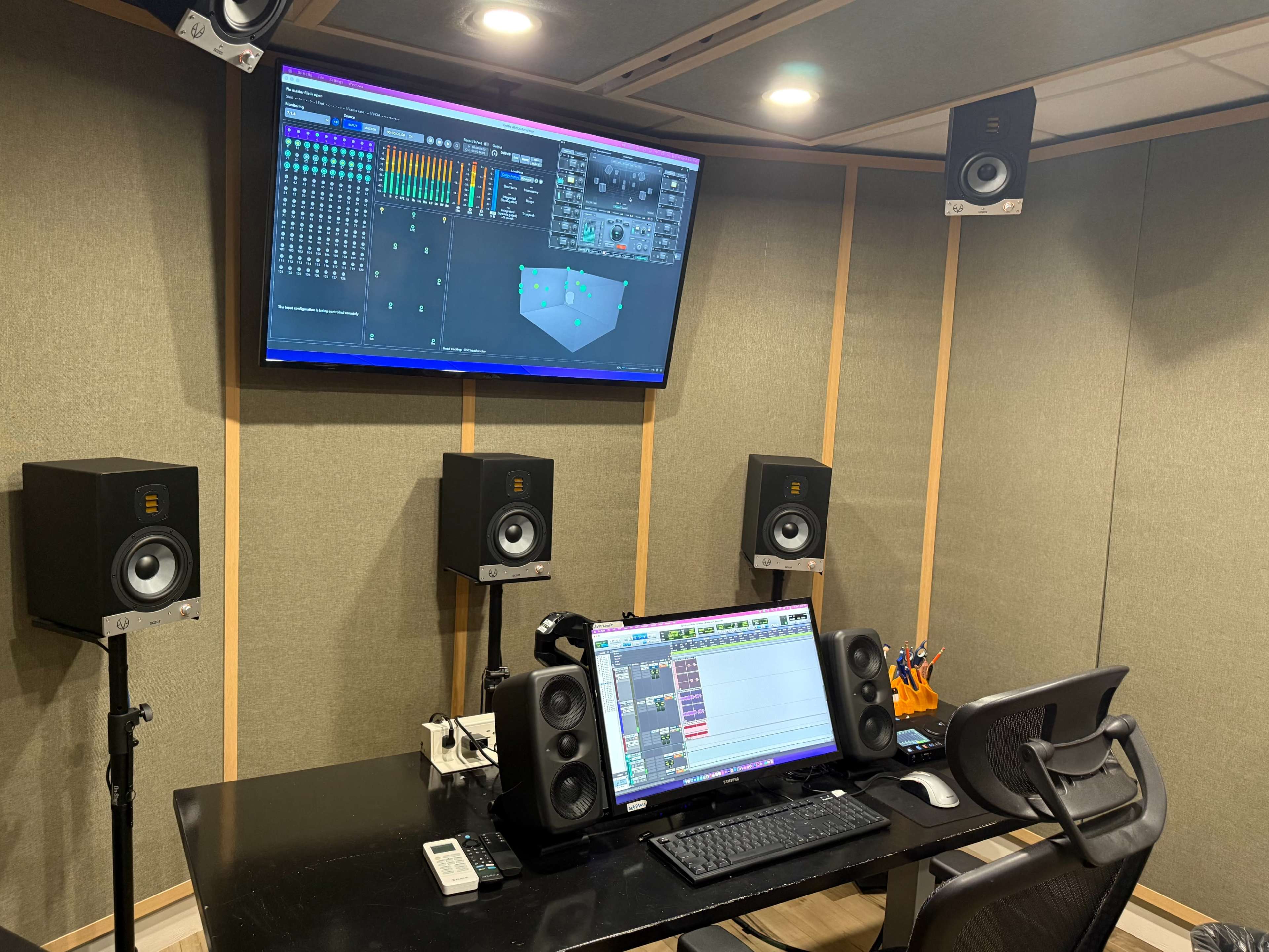 The image shows a sound studio featuring a mixing desk with speakers on either side, a computer monitor displaying audio software, and a carefully organized workspace.