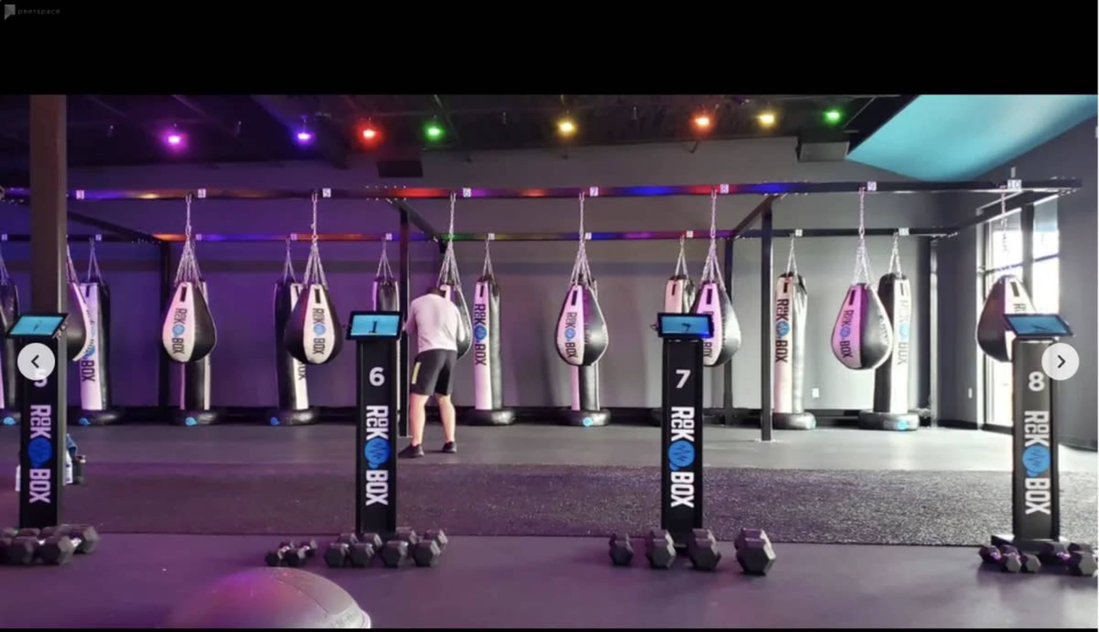 A gym interior features multiple suspended boxing bags and workout stations with numbered display screens along the floor.