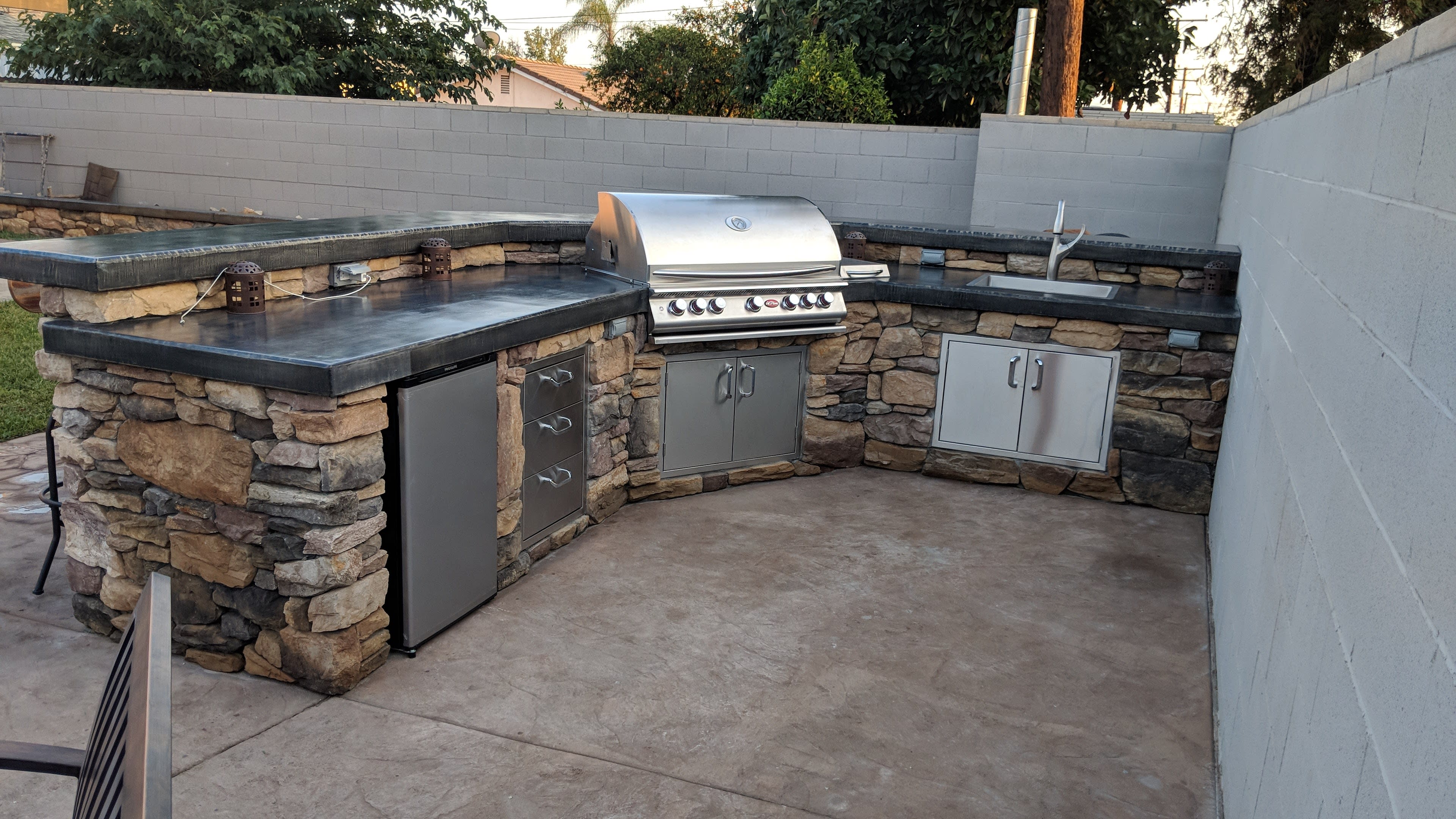 An outdoor kitchen with a stone and metal design, featuring a built-in grill, a sink, and storage cabinets.