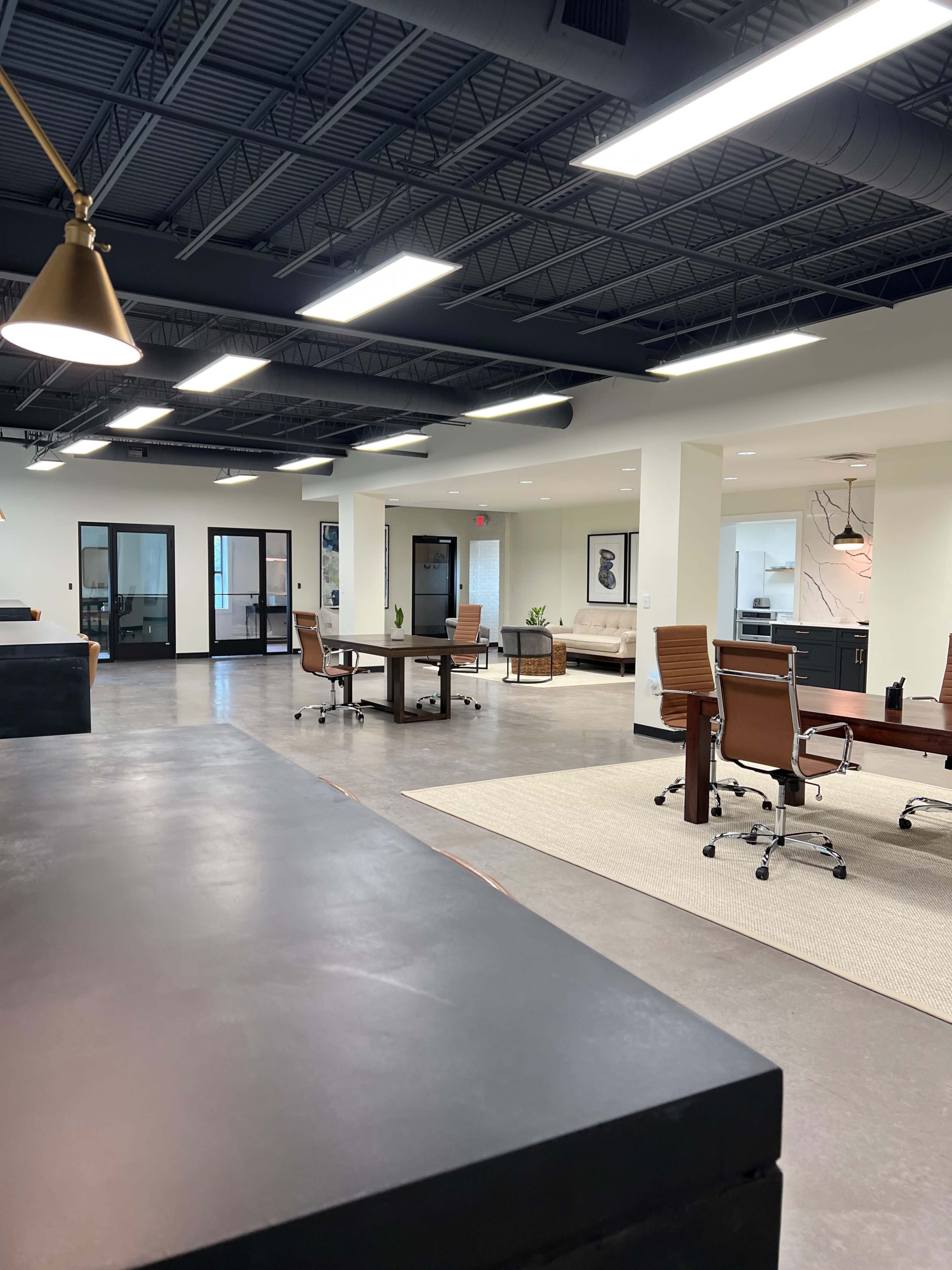 A modern open office space featuring several workstations, a conference area, and natural light streaming through large windows.