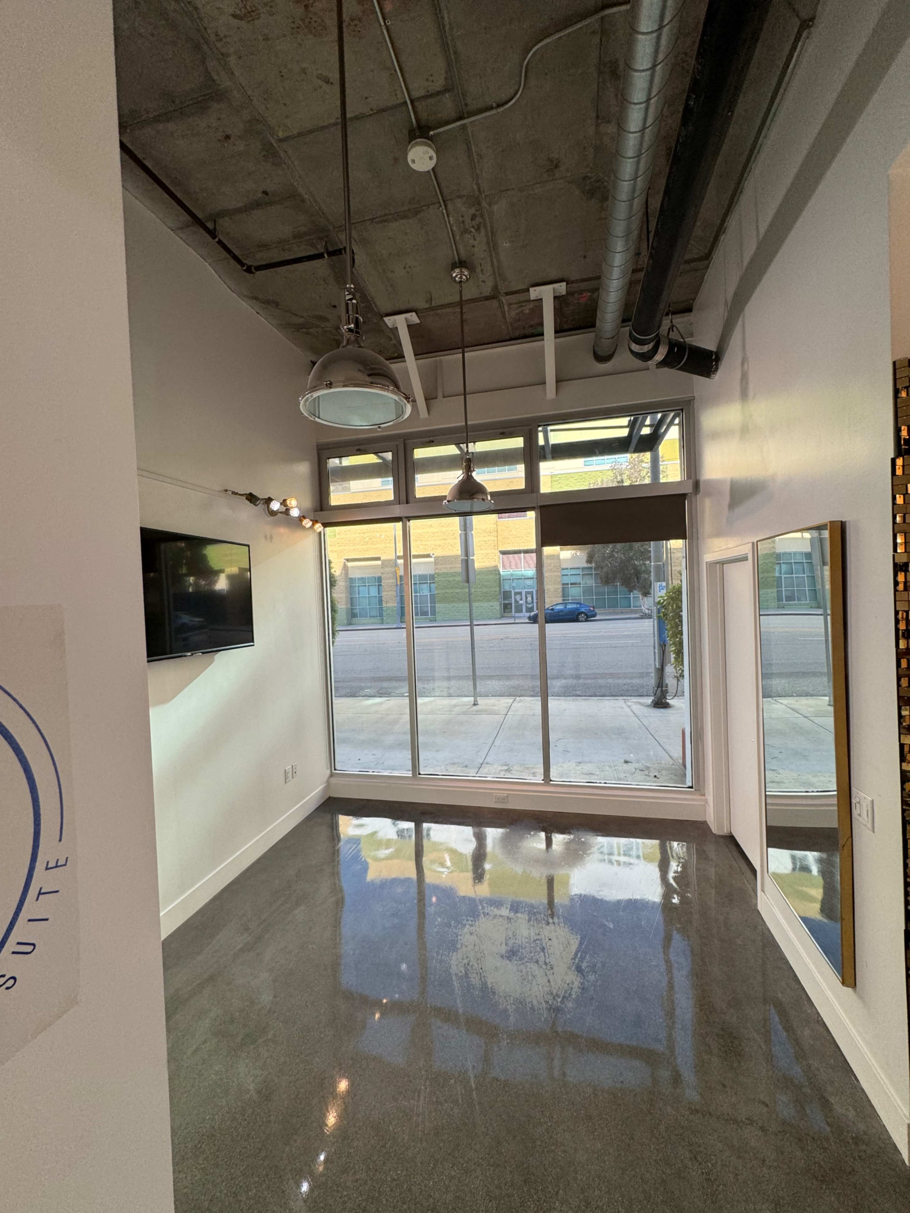 An empty interior space with polished concrete flooring, large windows facing the street, and modern lighting fixtures on the ceiling.
