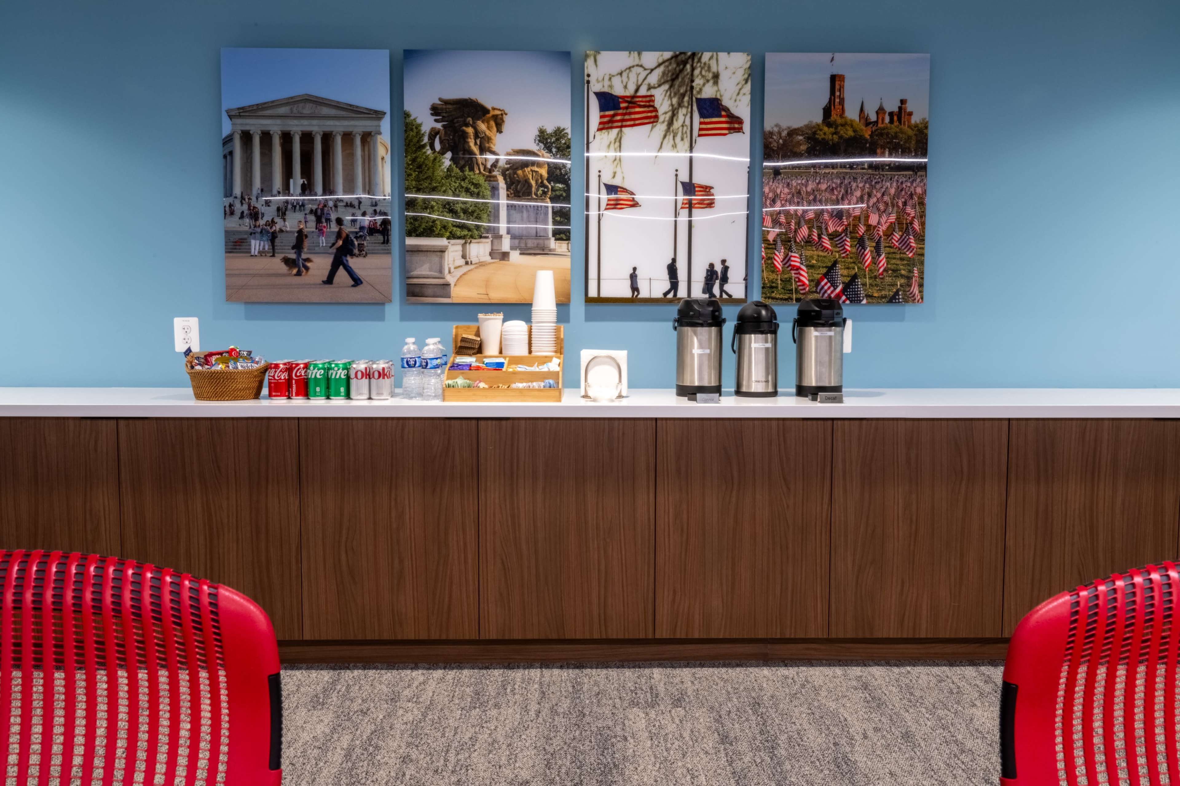 A beverage station with coffee pots and soft drinks is set against a backdrop of framed photographs featuring iconic American landmarks and flag displays.