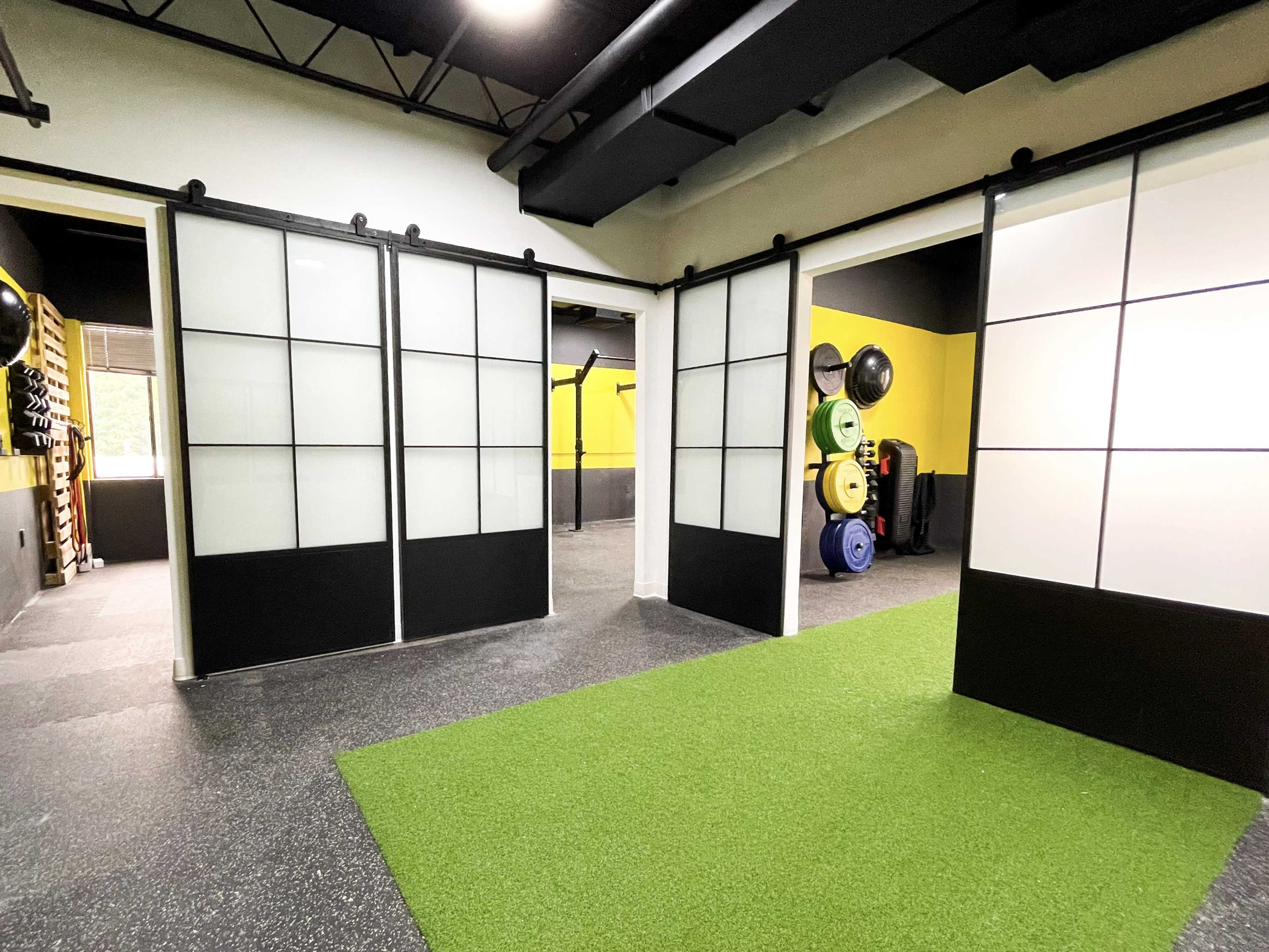 A modern gym interior featuring sliding glass doors, black and yellow walls, and exercise equipment arranged along one side.