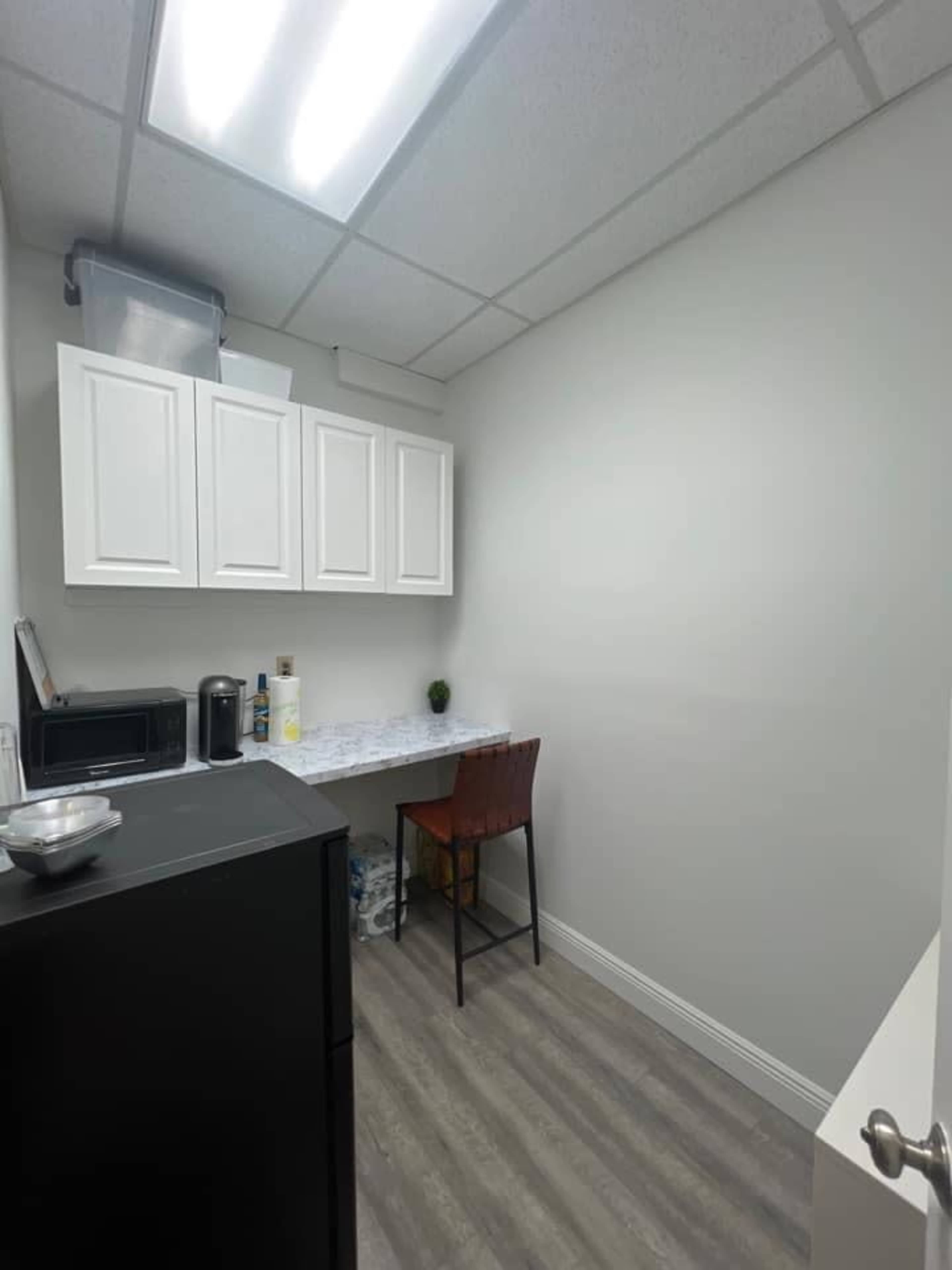 A small kitchen area with a black refrigerator, a microwave, white cabinets, and a wooden chair beside a countertop.