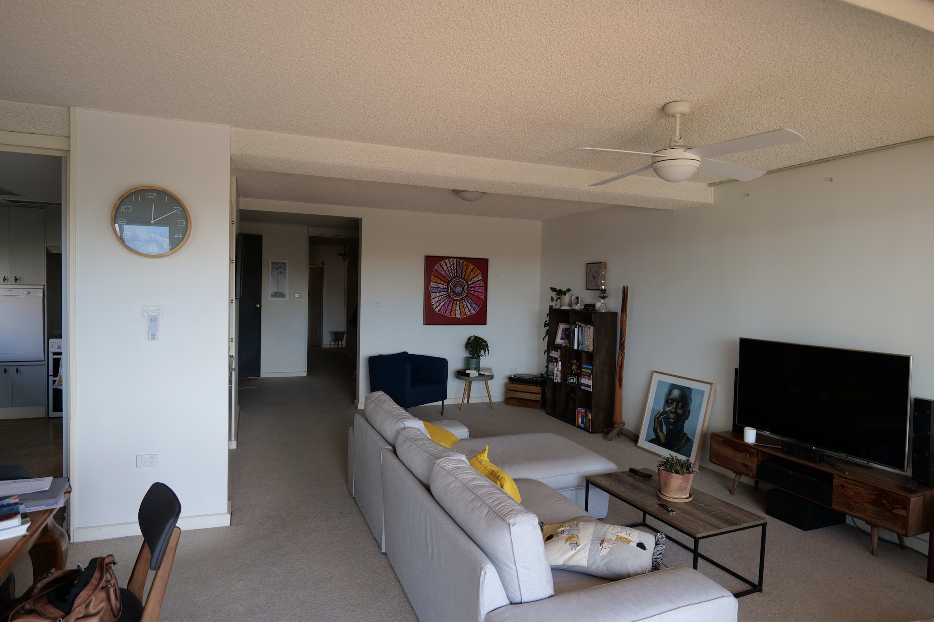 A spacious living room features a couch, coffee table, and television, with a clock on the wall and artwork displayed nearby.
