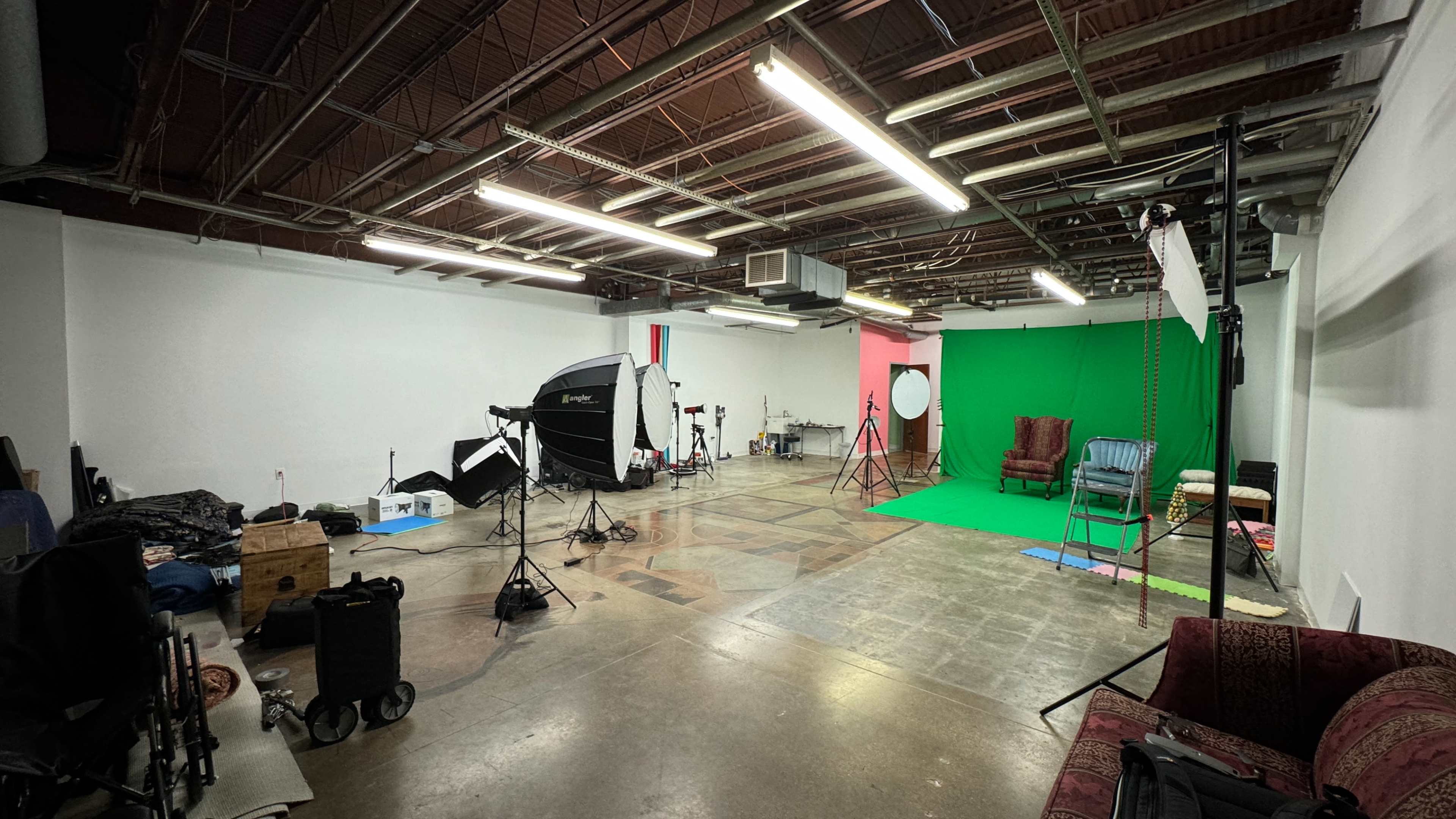 A photography studio with a green backdrop, lighting equipment, and various props scattered around.