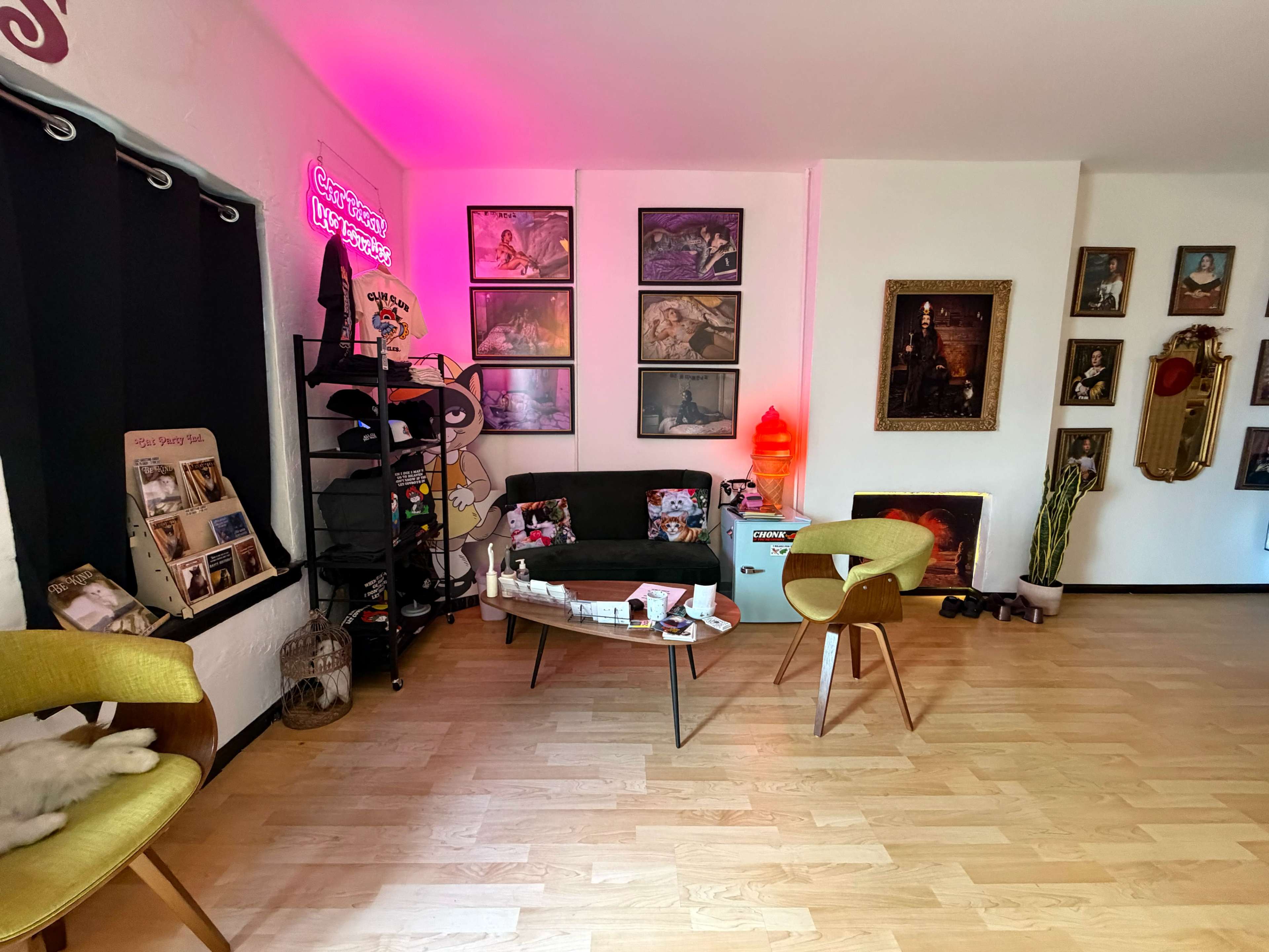 The room features a mix of wall art, a black couch, two chairs, and various decorative items on display.