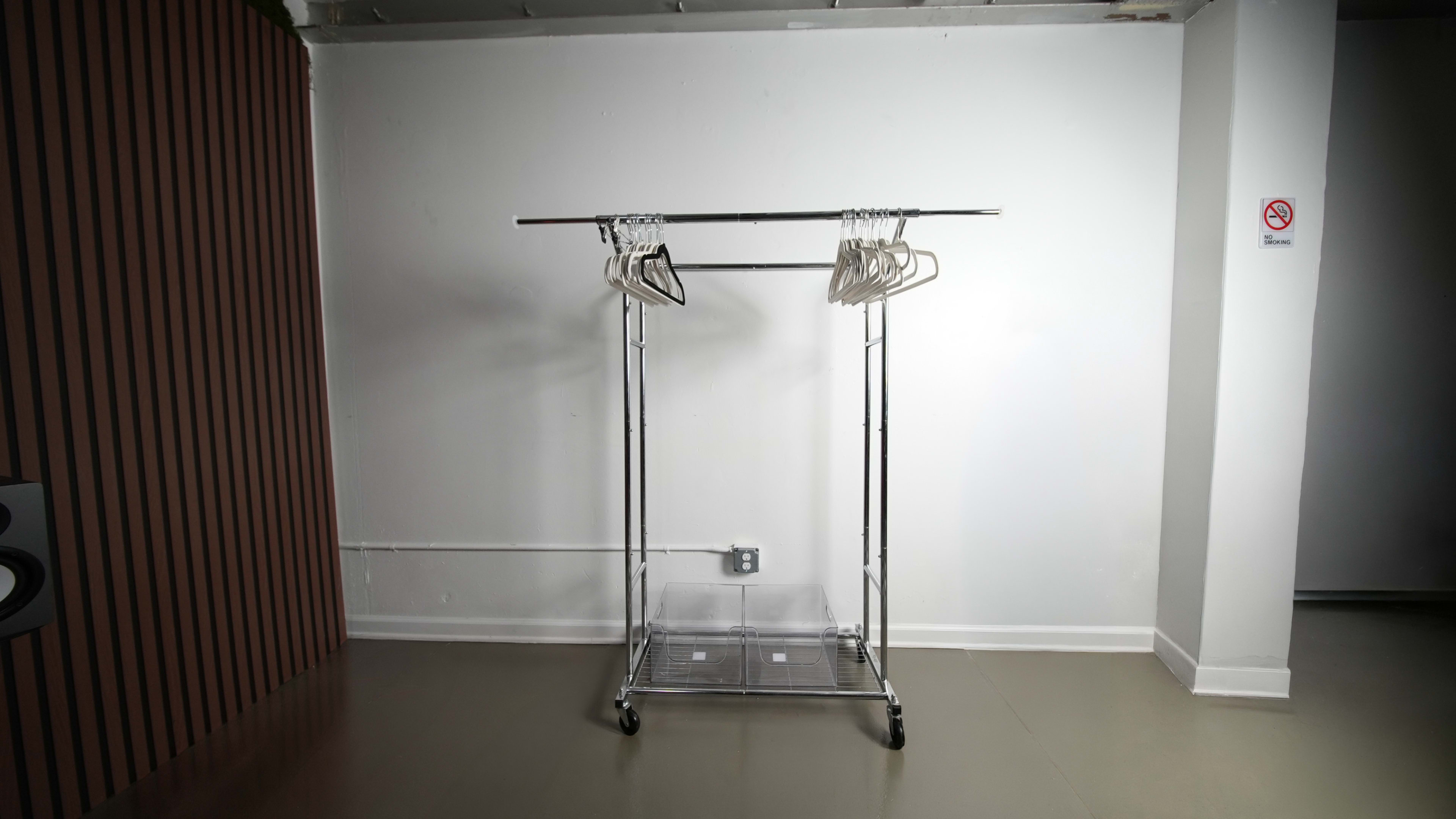 A metal clothing rack with several hangers stands empty against a plain wall in a sparsely decorated room.