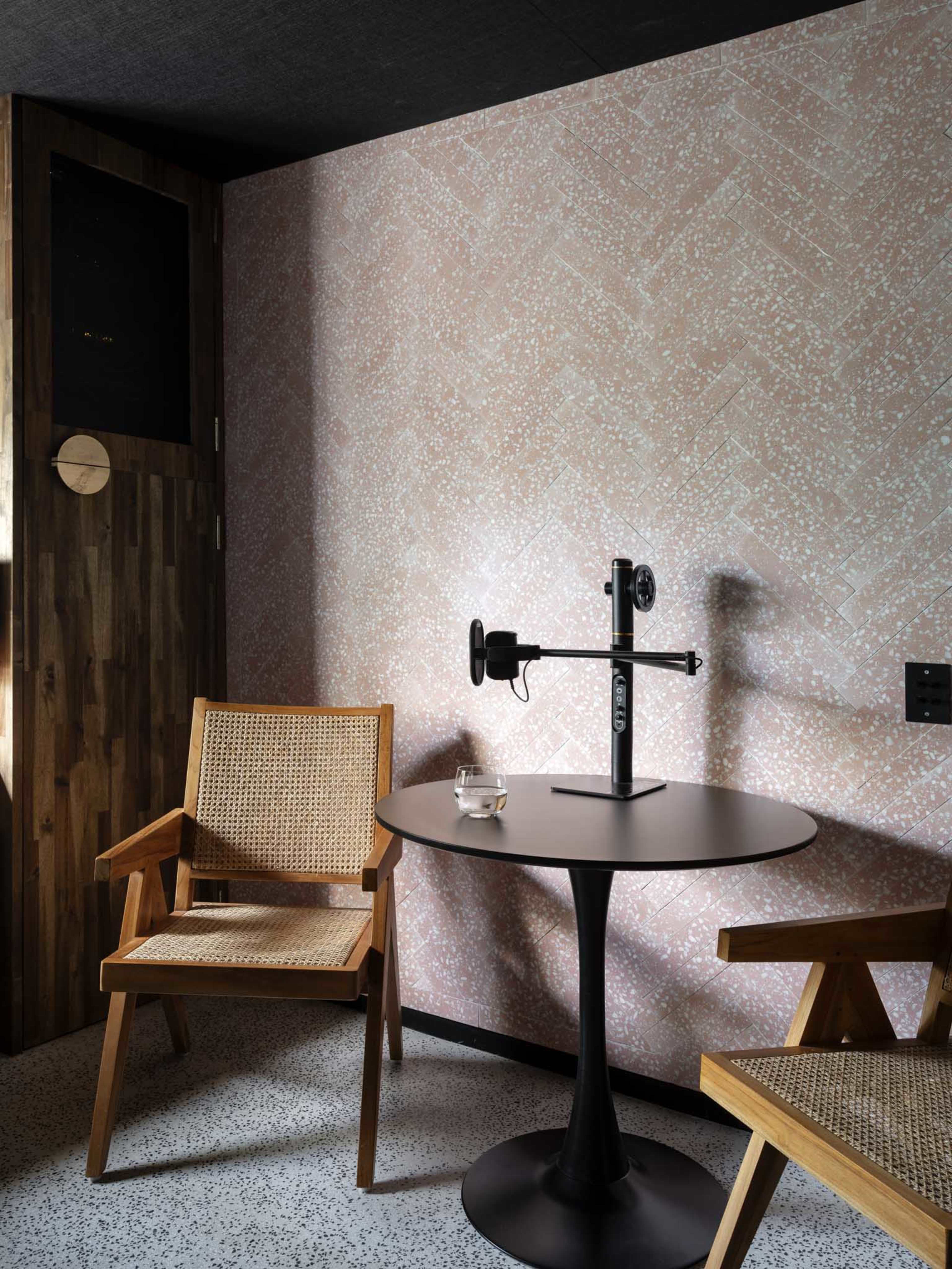 The image shows a cozy corner of a room featuring two wooden chairs, a round table, and a wall with a textured pink design.