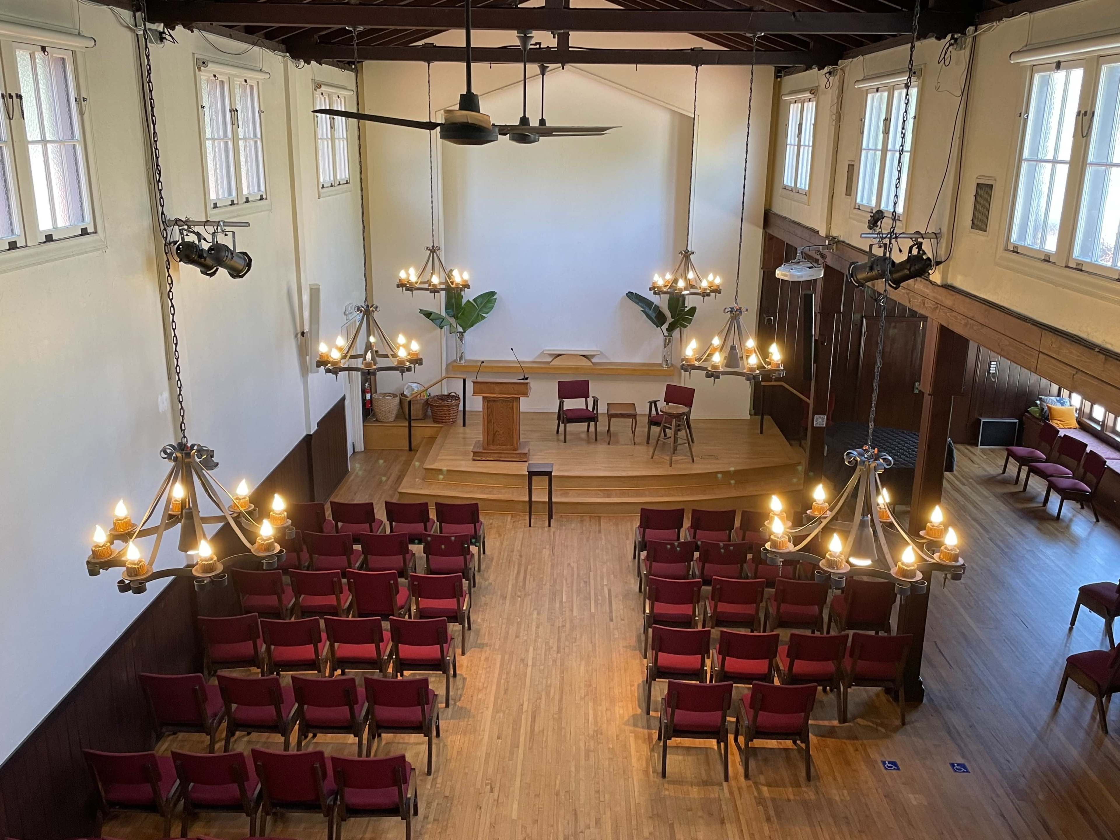 An elevated view of a seminar room with red chairs arranged in rows facing a wooden podium and two empty chairs on a raised platform.