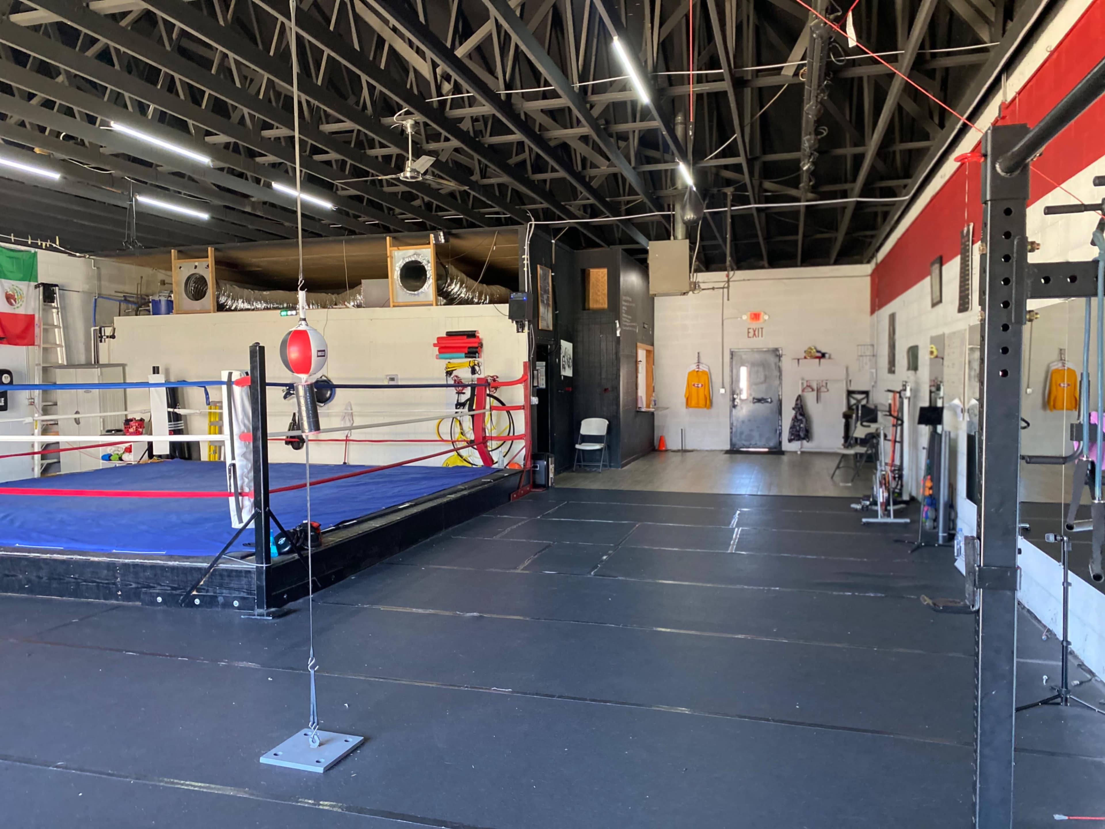 A boxing gym featuring a boxing ring with blue padding, a variety of equipment, and a spacious training area.