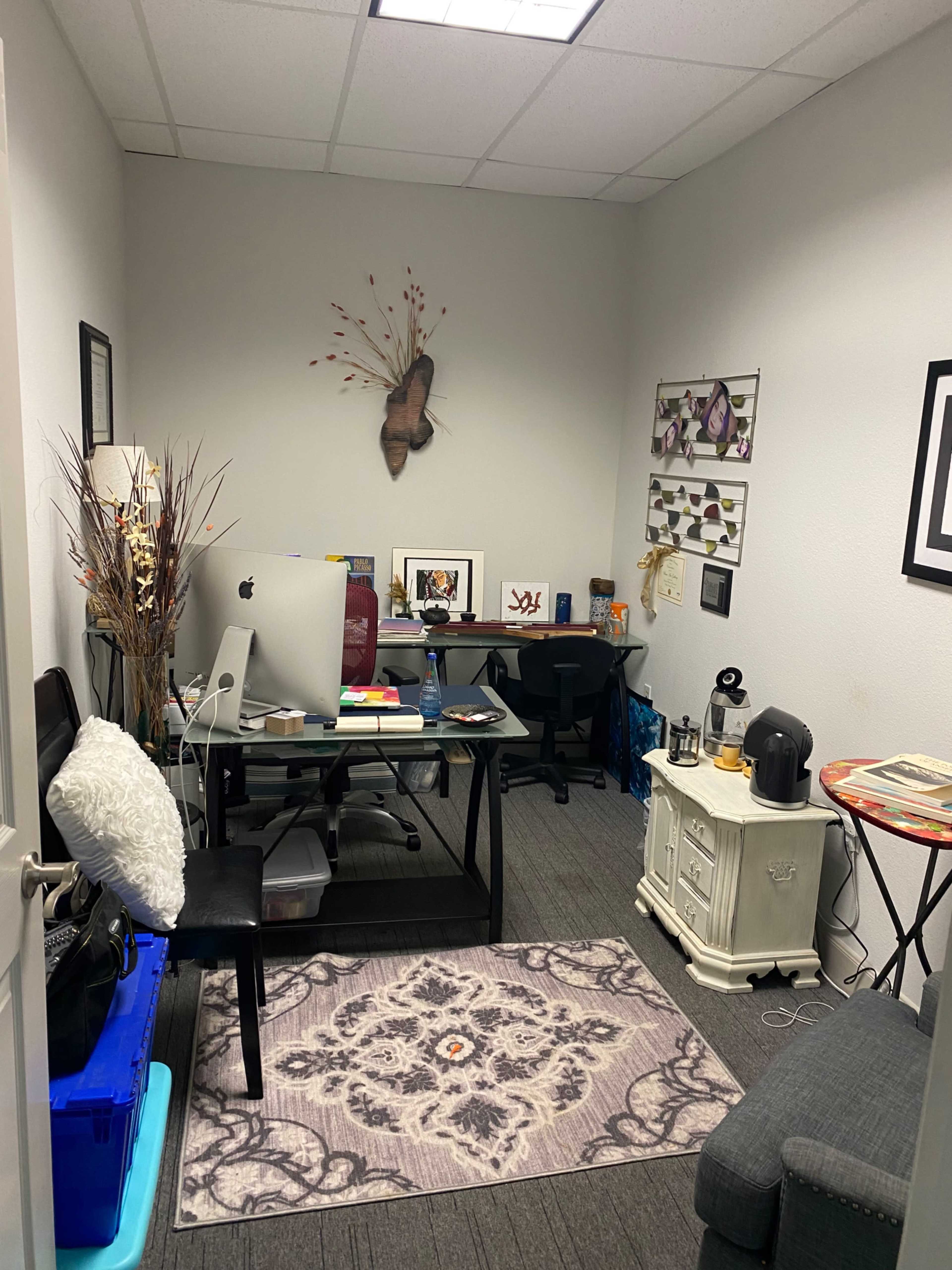 A small office space furnished with a desk, a computer, a chair, and decorative items on the walls.