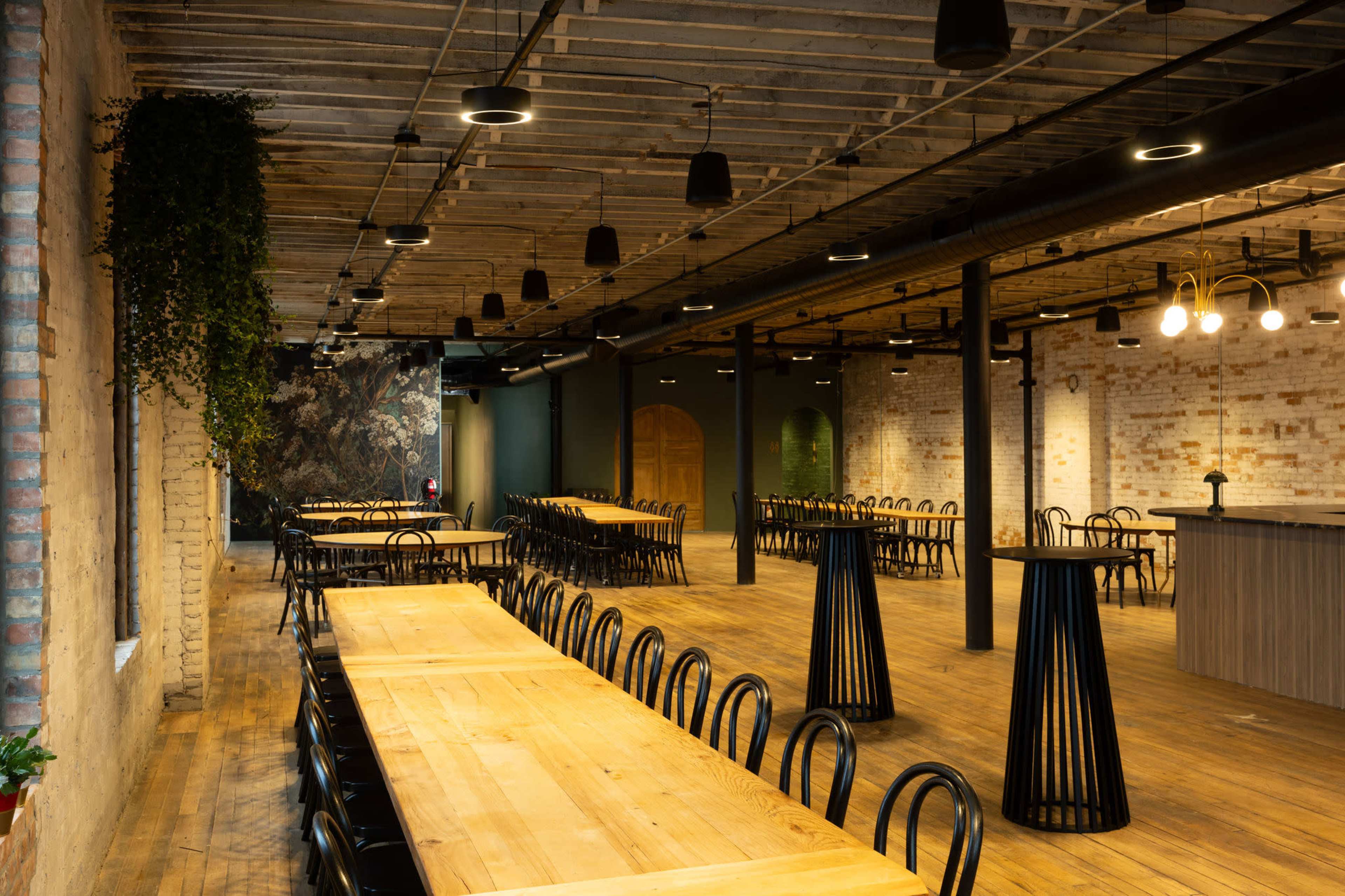 The image shows a spacious, industrial-style meeting room with long wooden tables and black chairs, featuring exposed brick walls and a wooden ceiling.