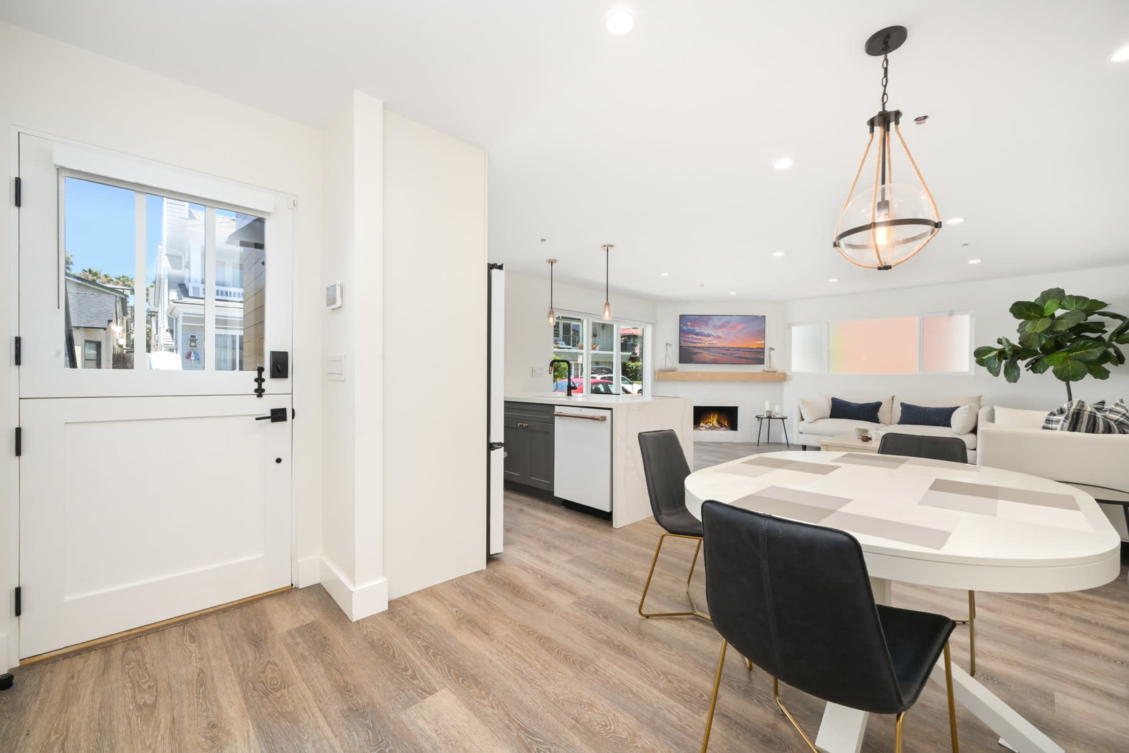 A modern interior space featuring a dining area with a round table and black chairs, a kitchen with gray cabinets, and a cozy living room with a sectional sofa and a wall-mounted television.