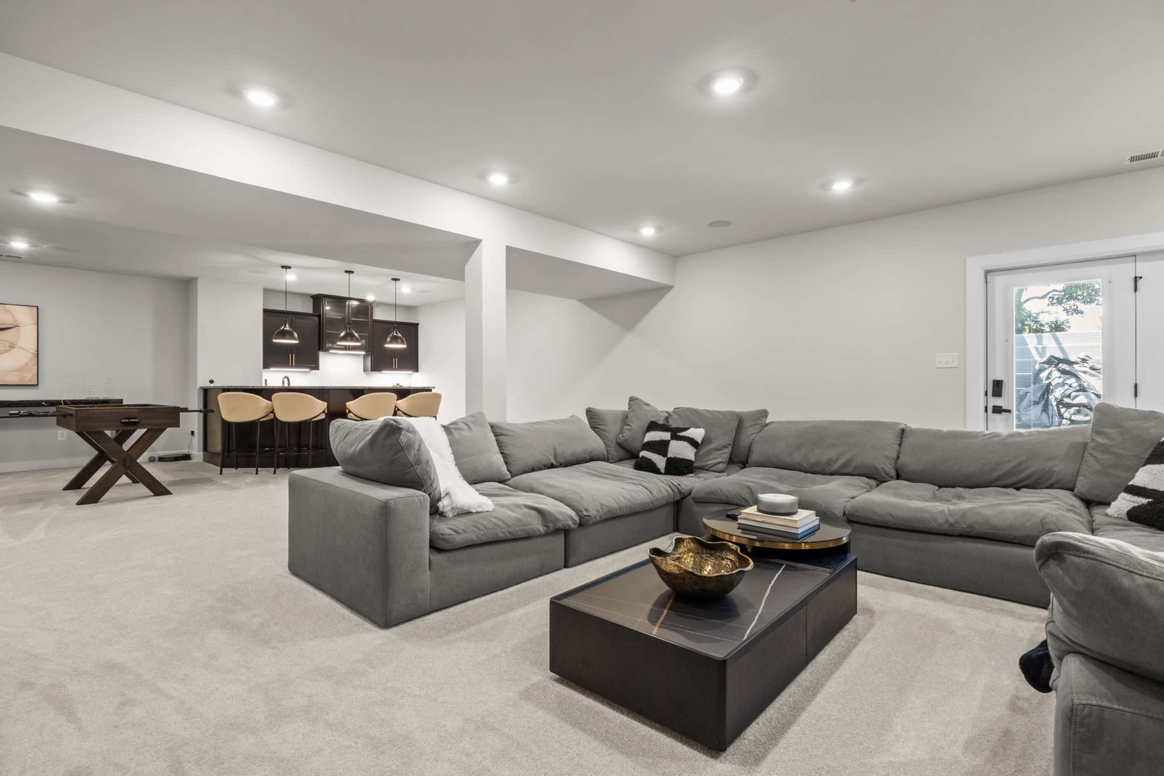 The image shows a modern living area with a large gray sectional sofa, a coffee table, and a bar area in the background.